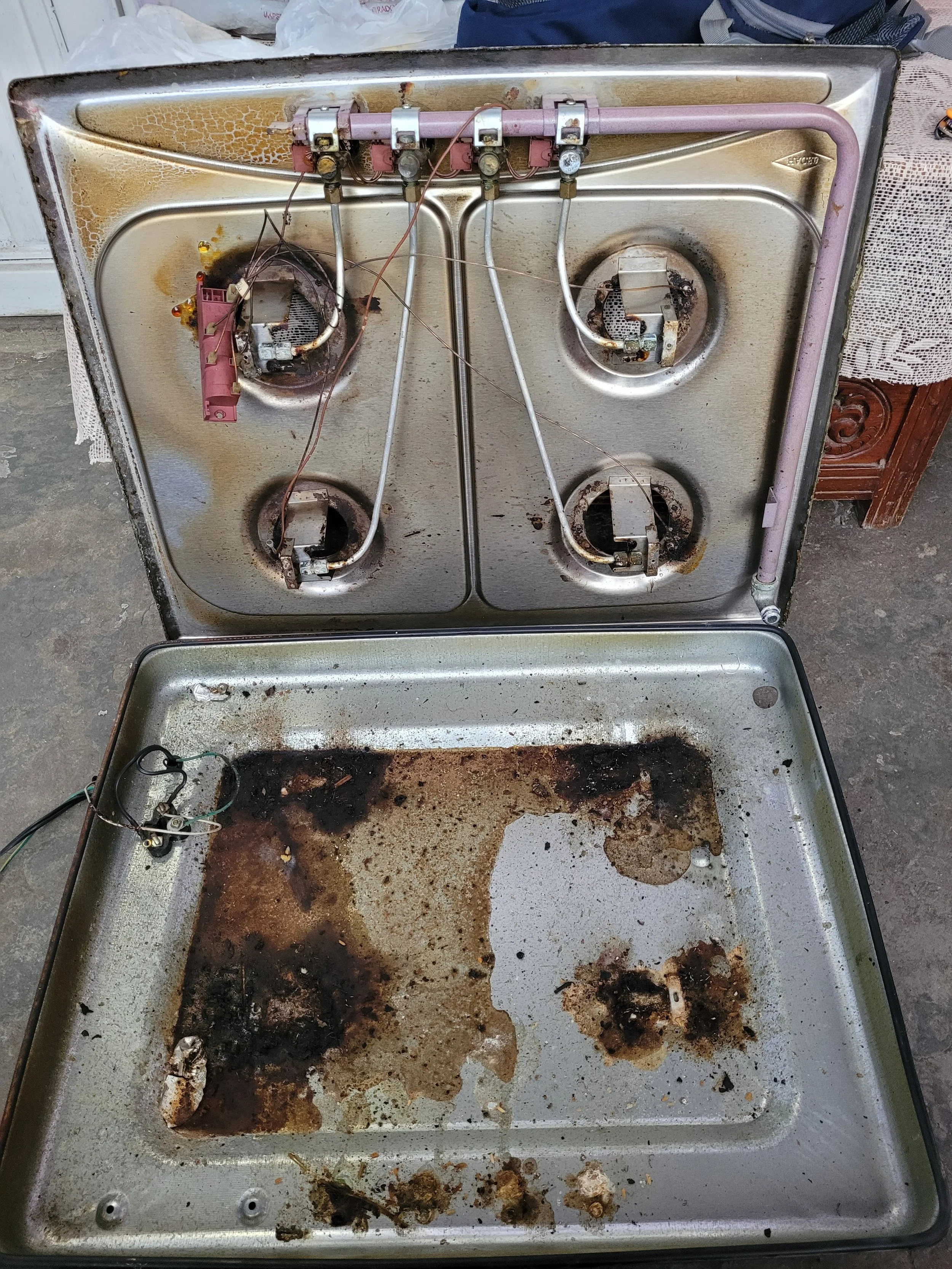 Un horno de estufa viejo y dañado con quemaduras y acumulación de suciedad en la superficie y en las hornallas.