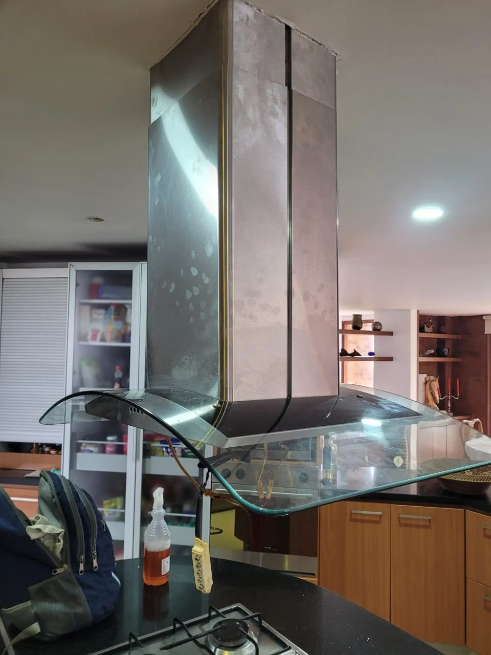 Campana extractora de cocina moderna instalada en el techo con un campana de vidrio en la base y un panel metálico vertical.