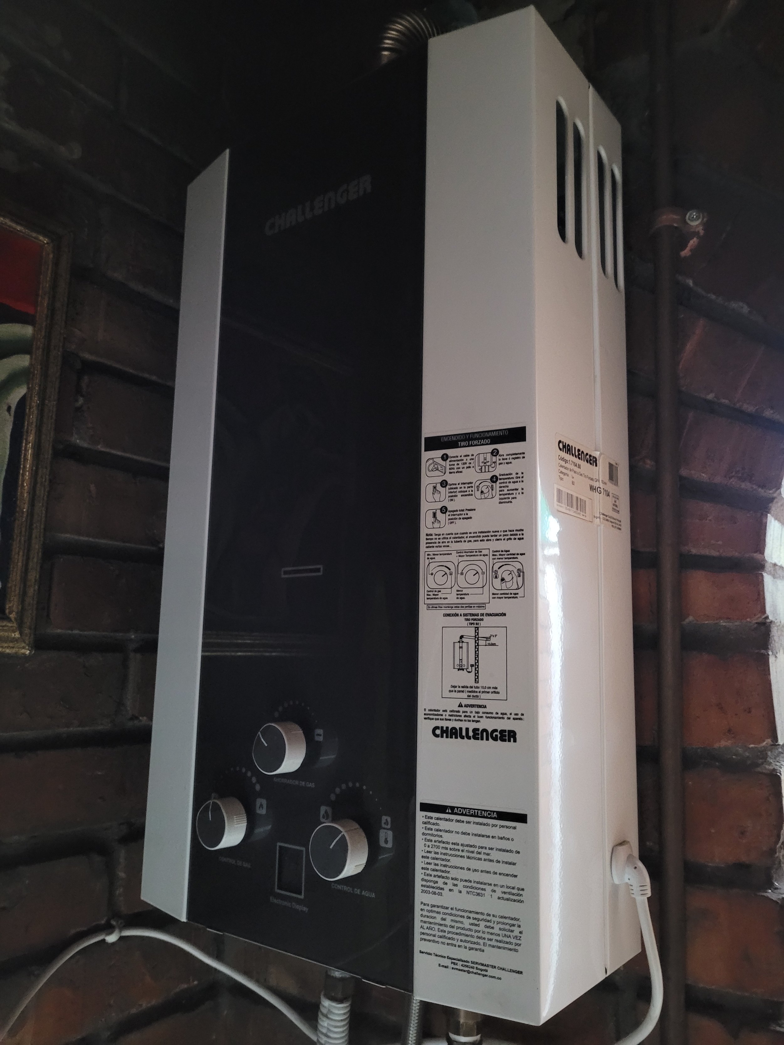 Calentador de agua marca Challenger instalado en una pared de ladrillos, con controles y etiquetas en español.
