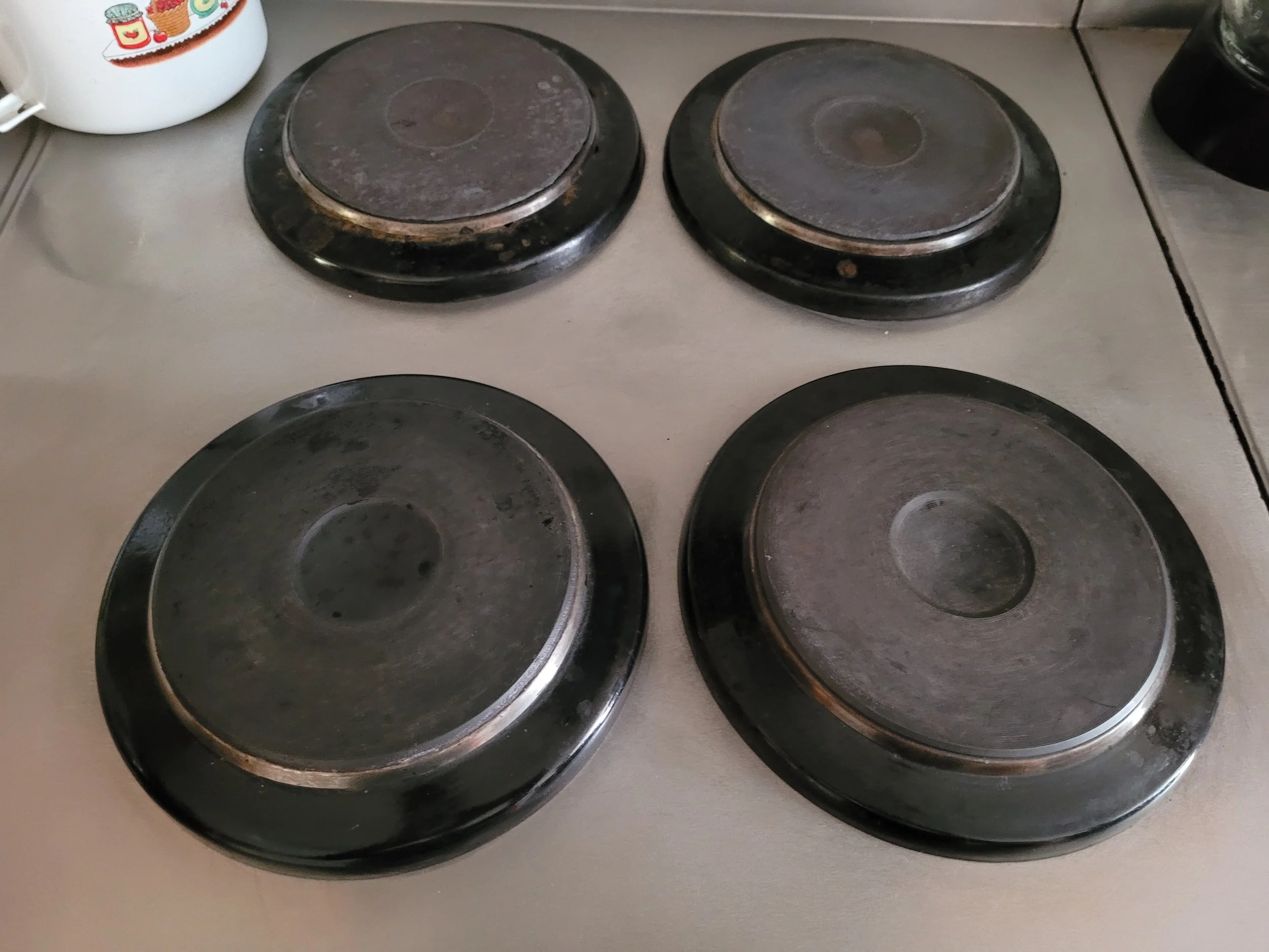 Cuatro quemadores eléctricos viejos, de color negro, en una encimera de cocina, con signos de uso y suciedad en las superficies.