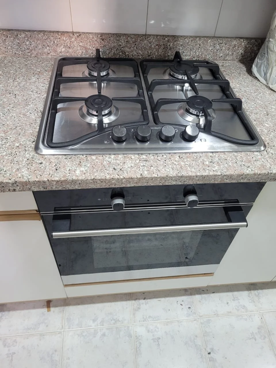 Estufa de gas de cuatro quemadores en una cocina con encimera de granito y horno eléctrico debajo.