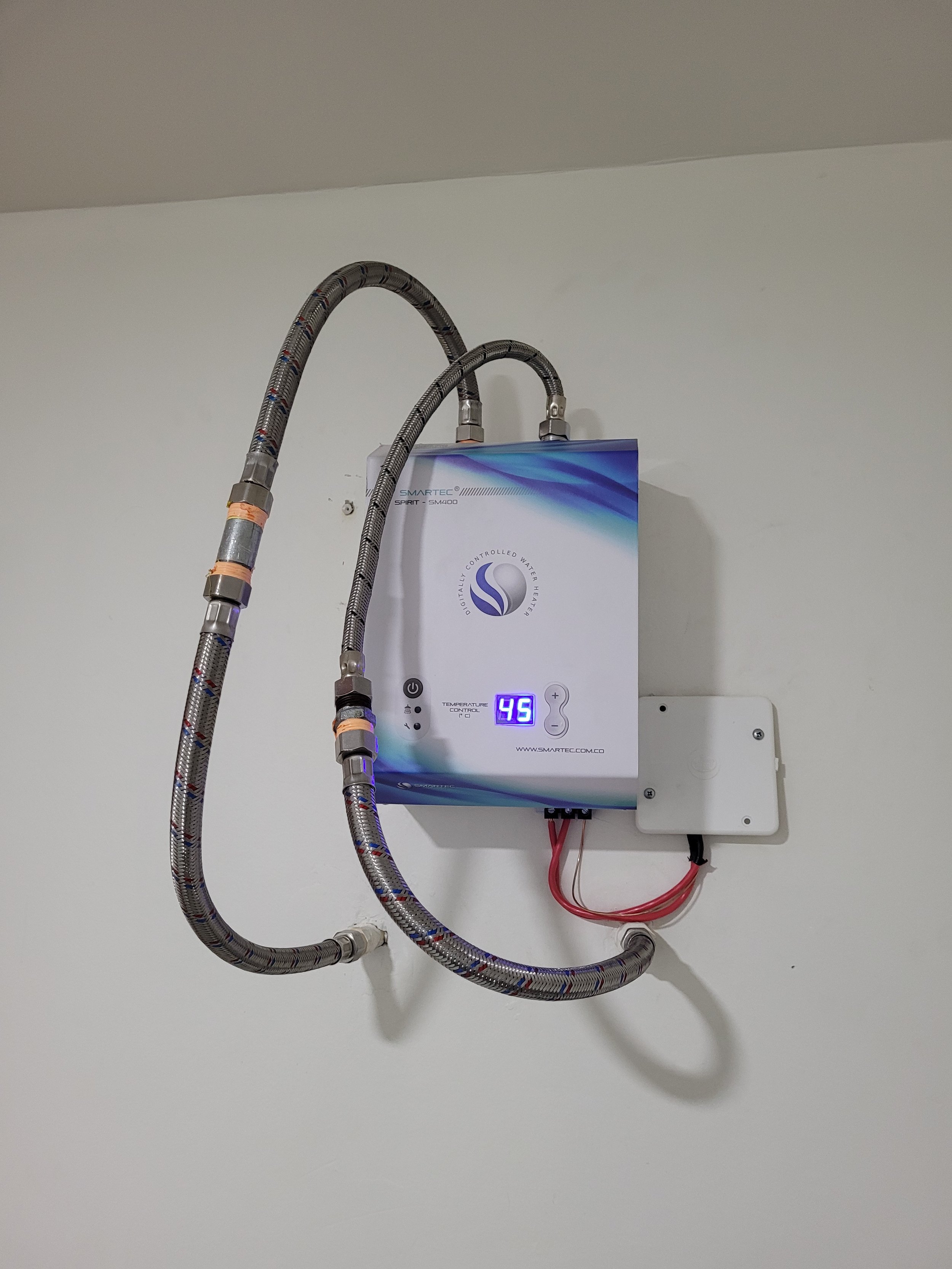 Sistema de purificación de agua con display digital, conectado a la pared con tubos y cables.