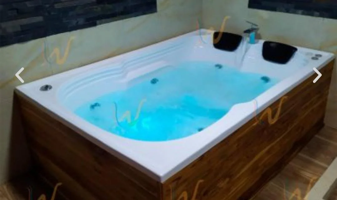 Jacuzzi con chorros de agua en una esquina de una habitación, rodeado por paredes y con una estructura de madera en su exterior.