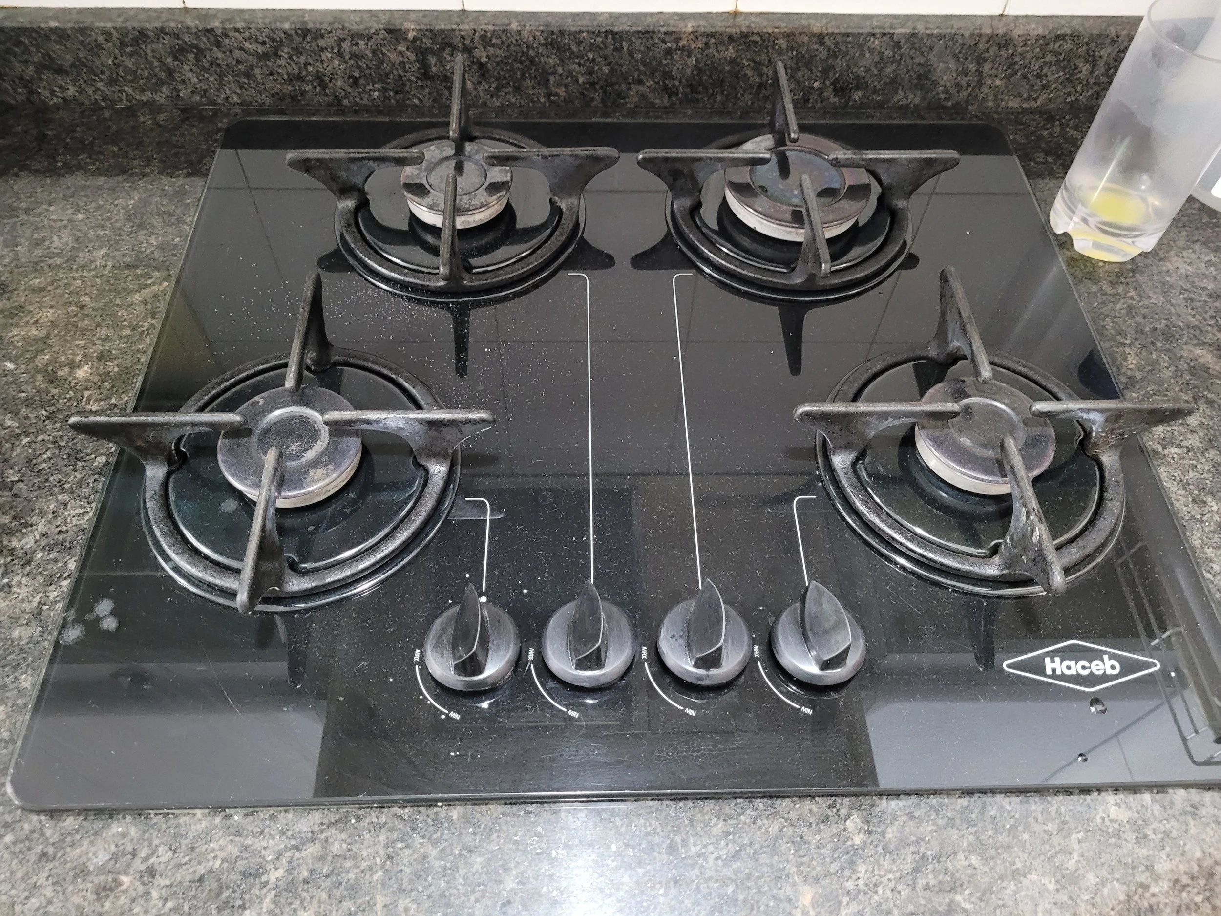 Estufa de vidrio con cuatro quemadores y controles de temperatura, en una encimera de cocina de granito oscuro.