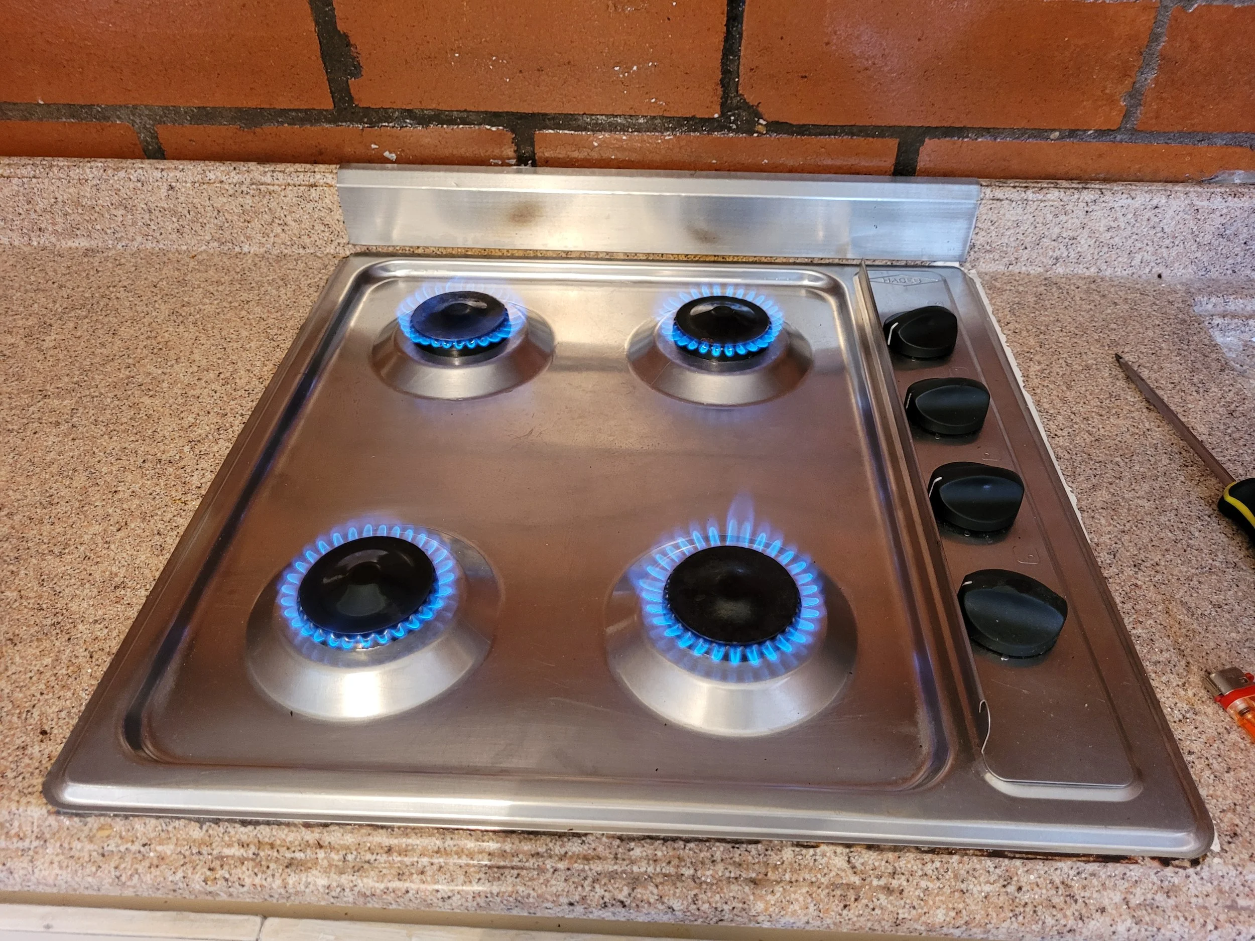 Estufa de gas de cuatro quemadores encendidos en una encimera de granito y fondo de ladrillos.