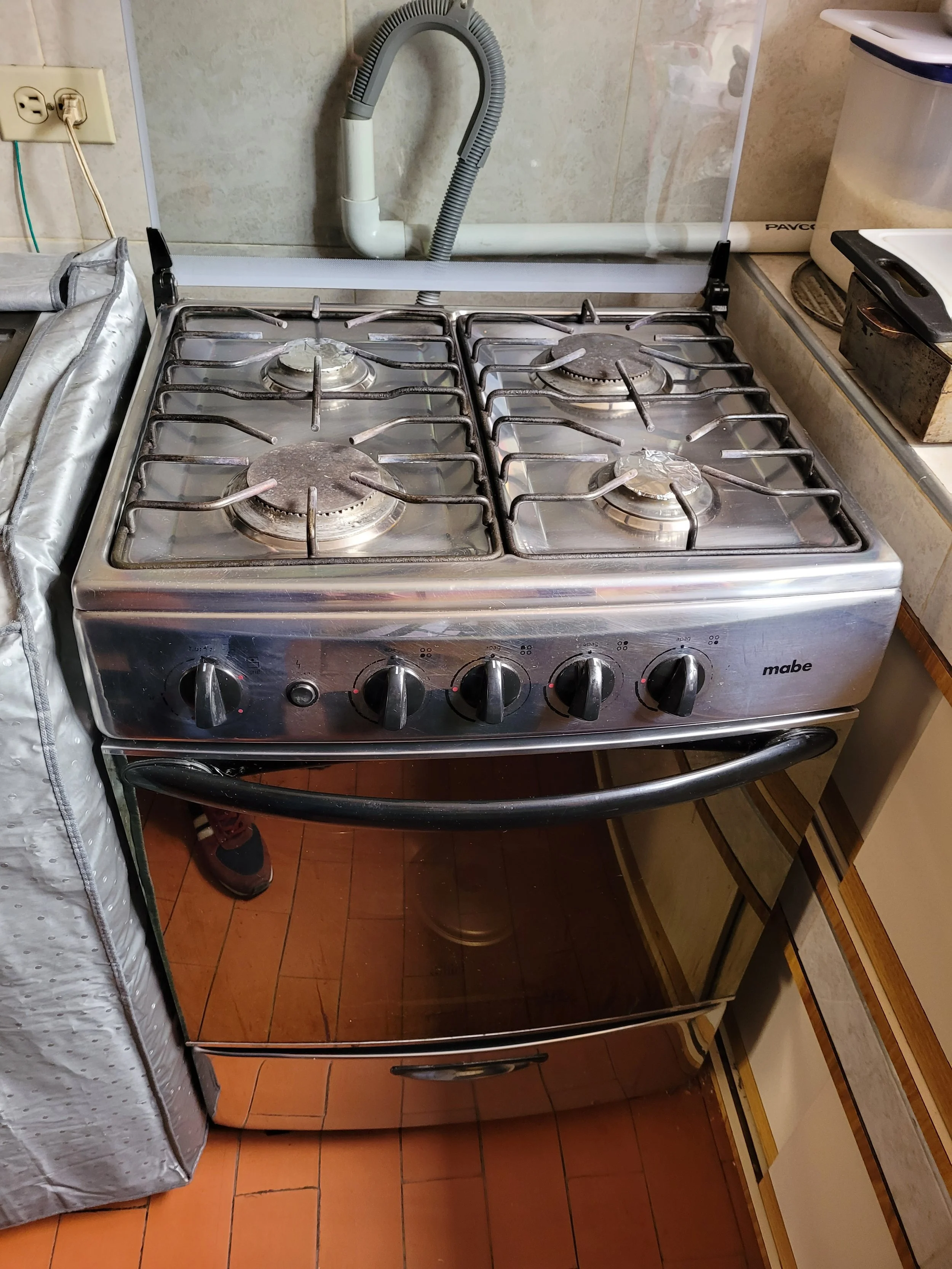 Estufa de cocina de tamaño estándar de seis quemadores de acero inoxidable con control de knobs en frente, en una cocina con piso de azulejos color terracota.