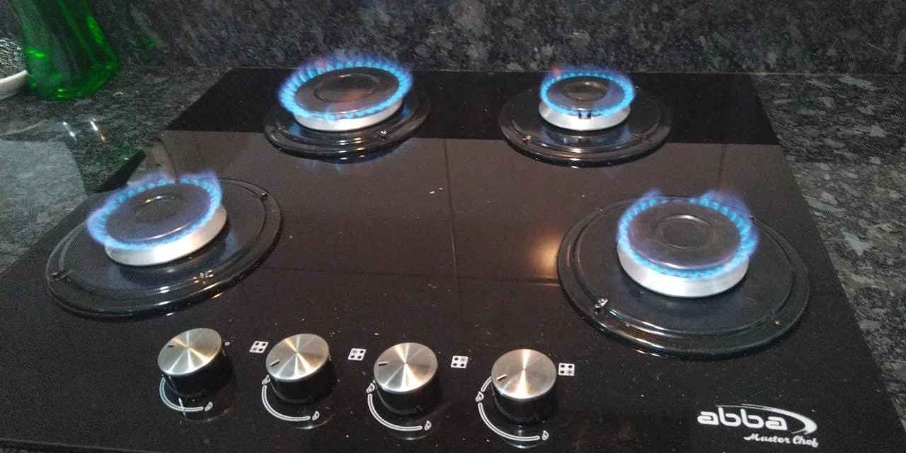 Estufa de gas con cuatro quemadores encendidos, con llamas azules y controles ajustados.