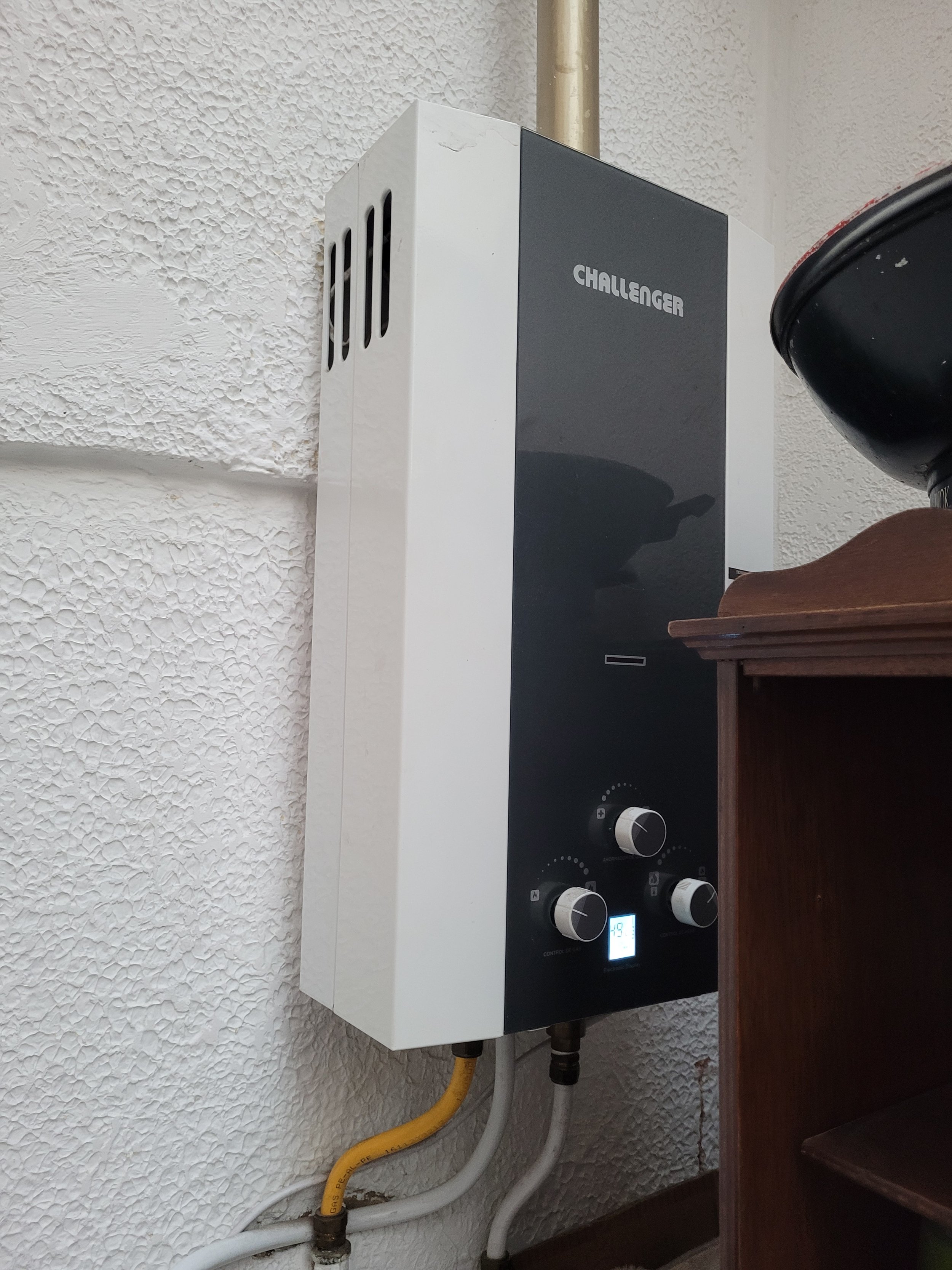 Aparato de calentador de agua Challenger montado en la pared junto a mangueras de entrada y salida de agua.