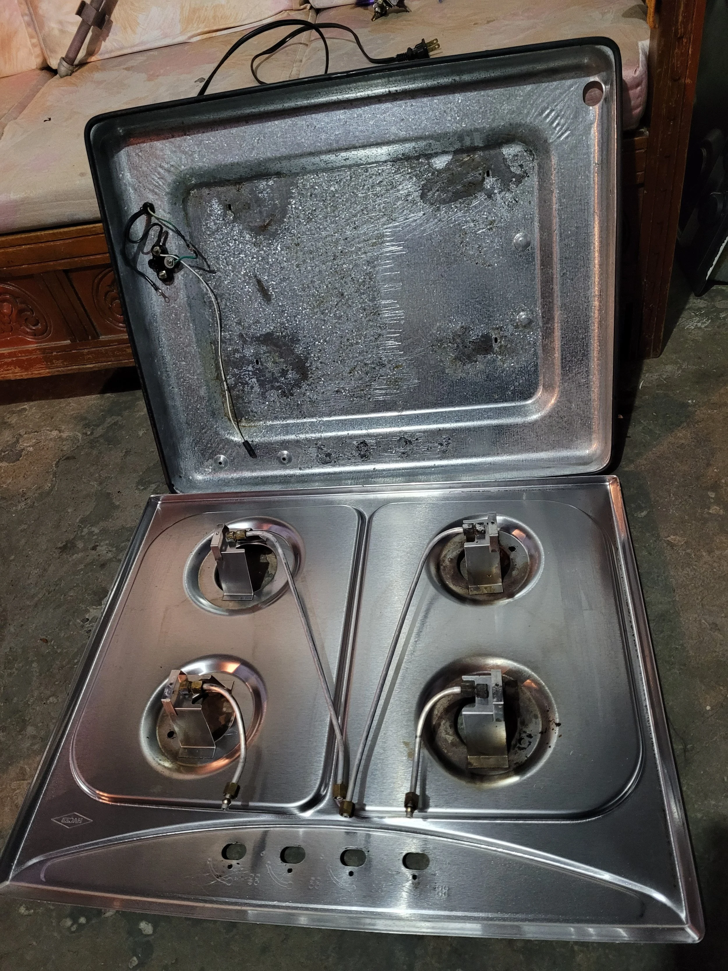 Estufa de cocina de gas sin quemadores, con la tapa abierta mostrando el interior sucio y desgastado.