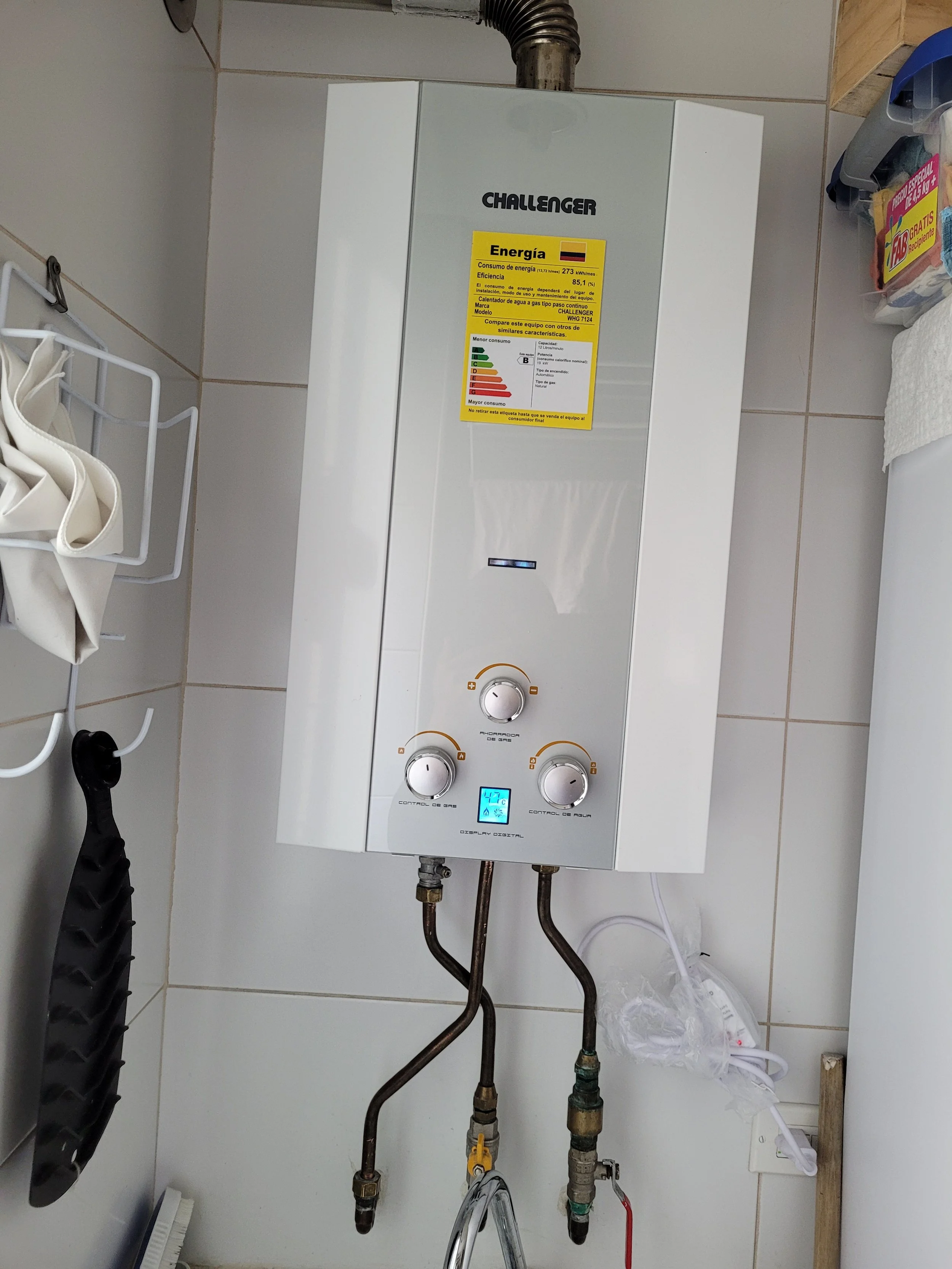 Calentador de agua blanco de la marca Challenger con controles y pantalla digital, instalado en una pared de azulejos, con una etiqueta de eficiencia energética.