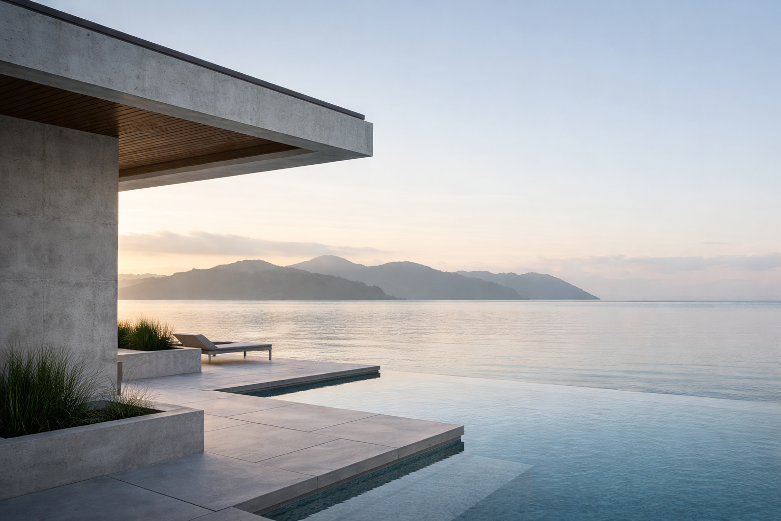 Modern house with a concrete exterior and an infinity pool overlooking a calm body of water and distant mountains during sunset.