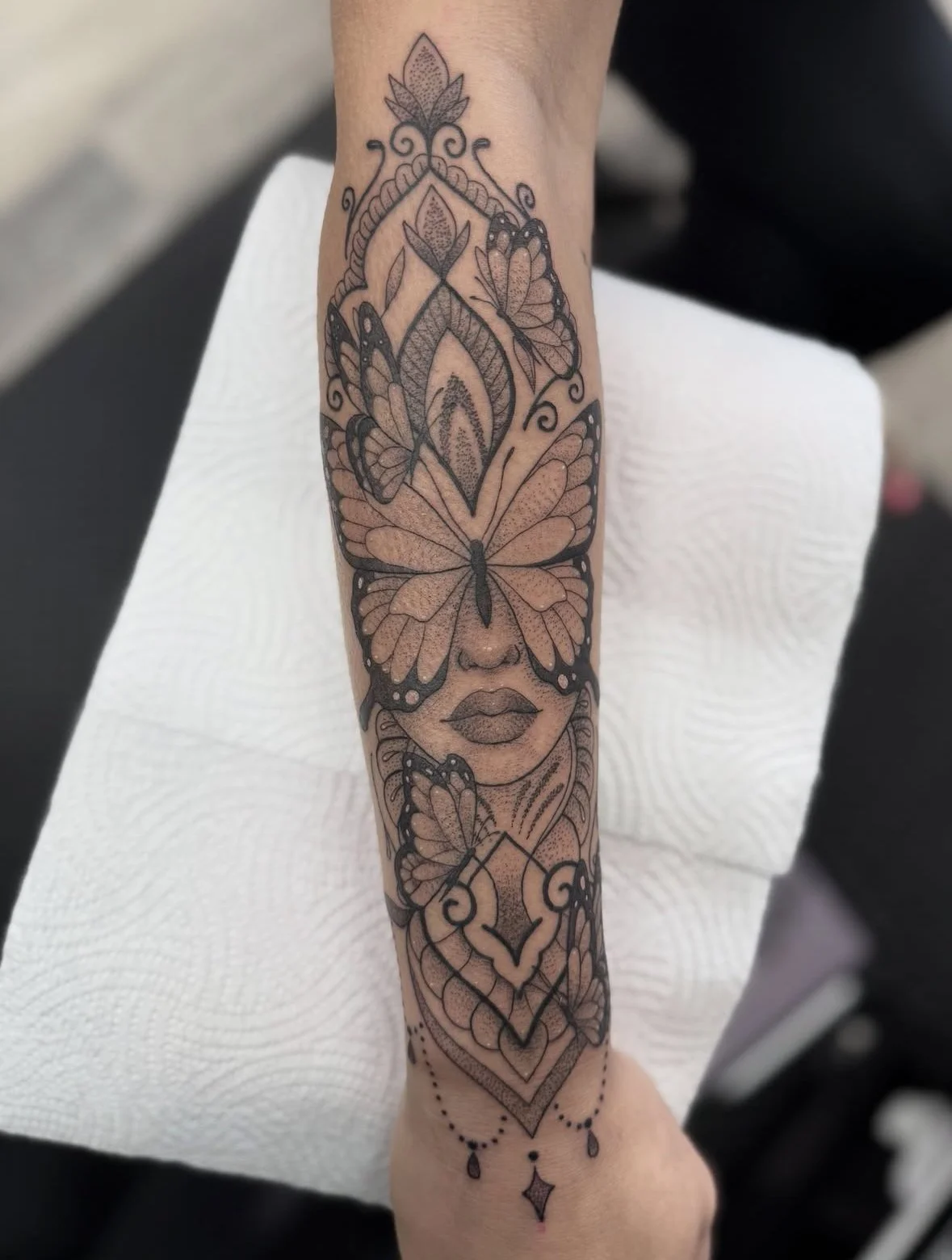 Tattoo of a woman's face with her eyes closed, surrounded by butterflies and floral designs, in black ink with detailed shading.