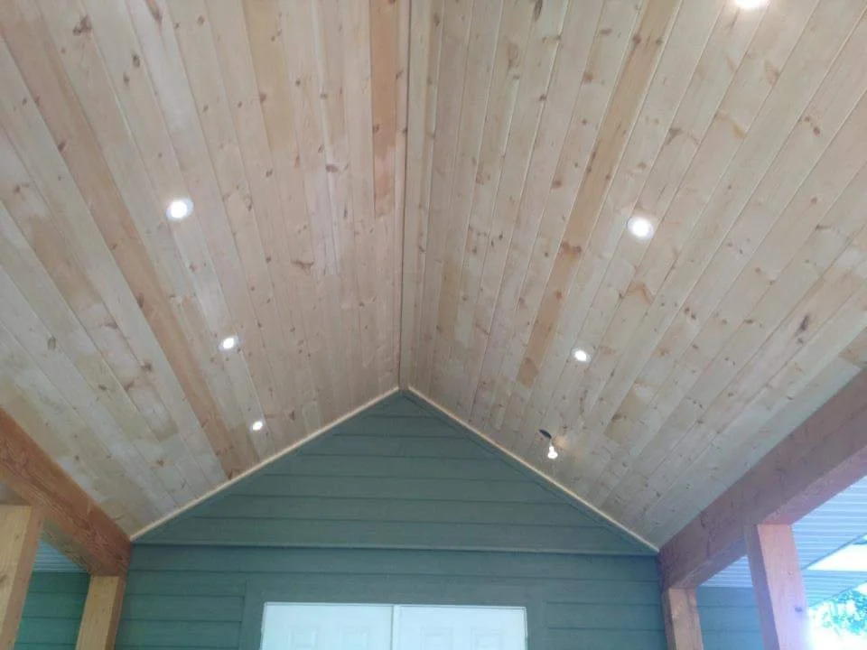 Interior view of a wooden ceiling with recessed lighting, part of a house with green walls and exposed wooden beams.