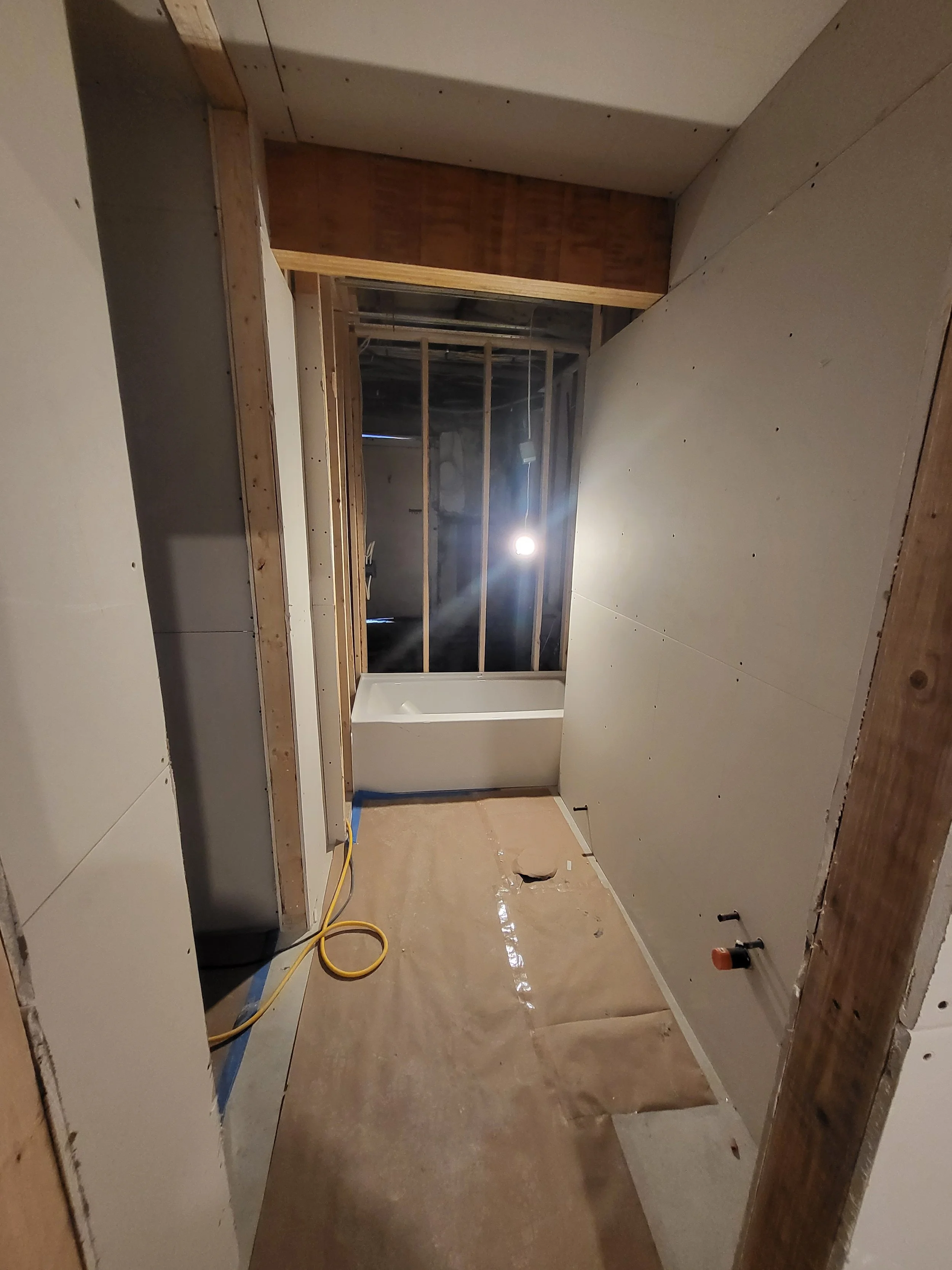 Bathroom under construction with drywall installed, wooden framing, a bathtub, and a construction light.