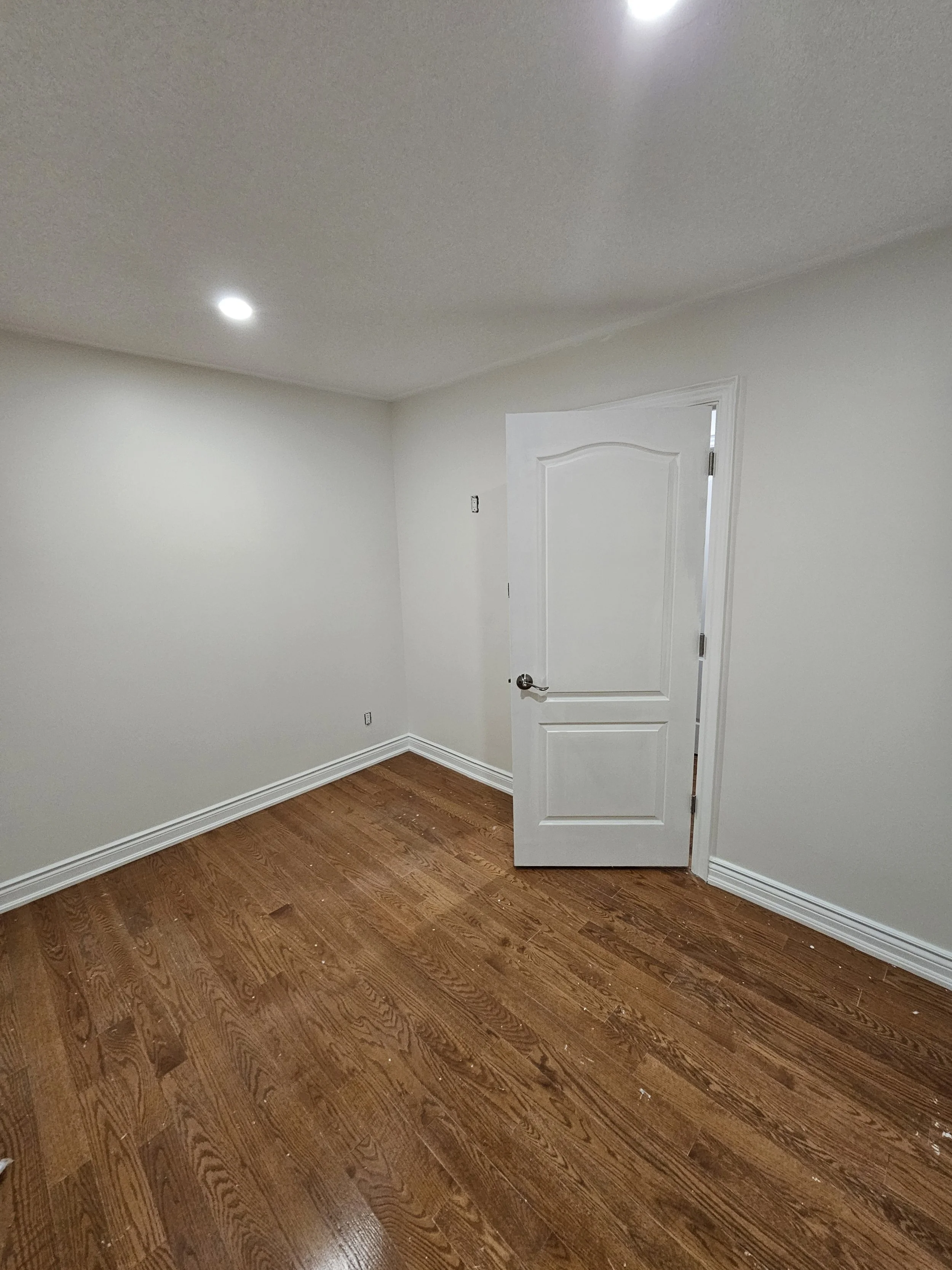 Empty room with white walls, ceiling lights, hardwood floor, and an open door