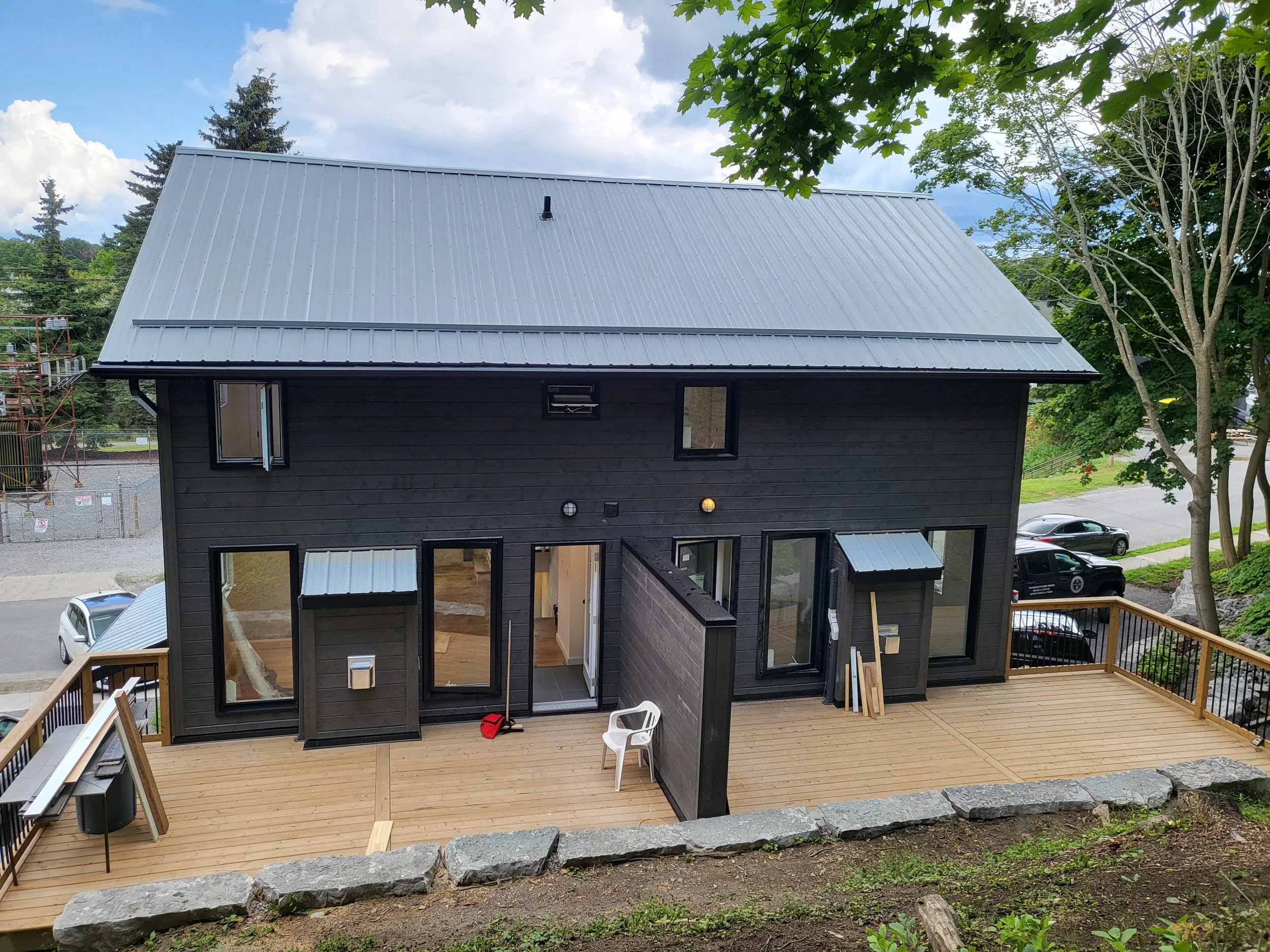 A black two-story house with a silver metal roof, surrounded by trees and a wooden deck.