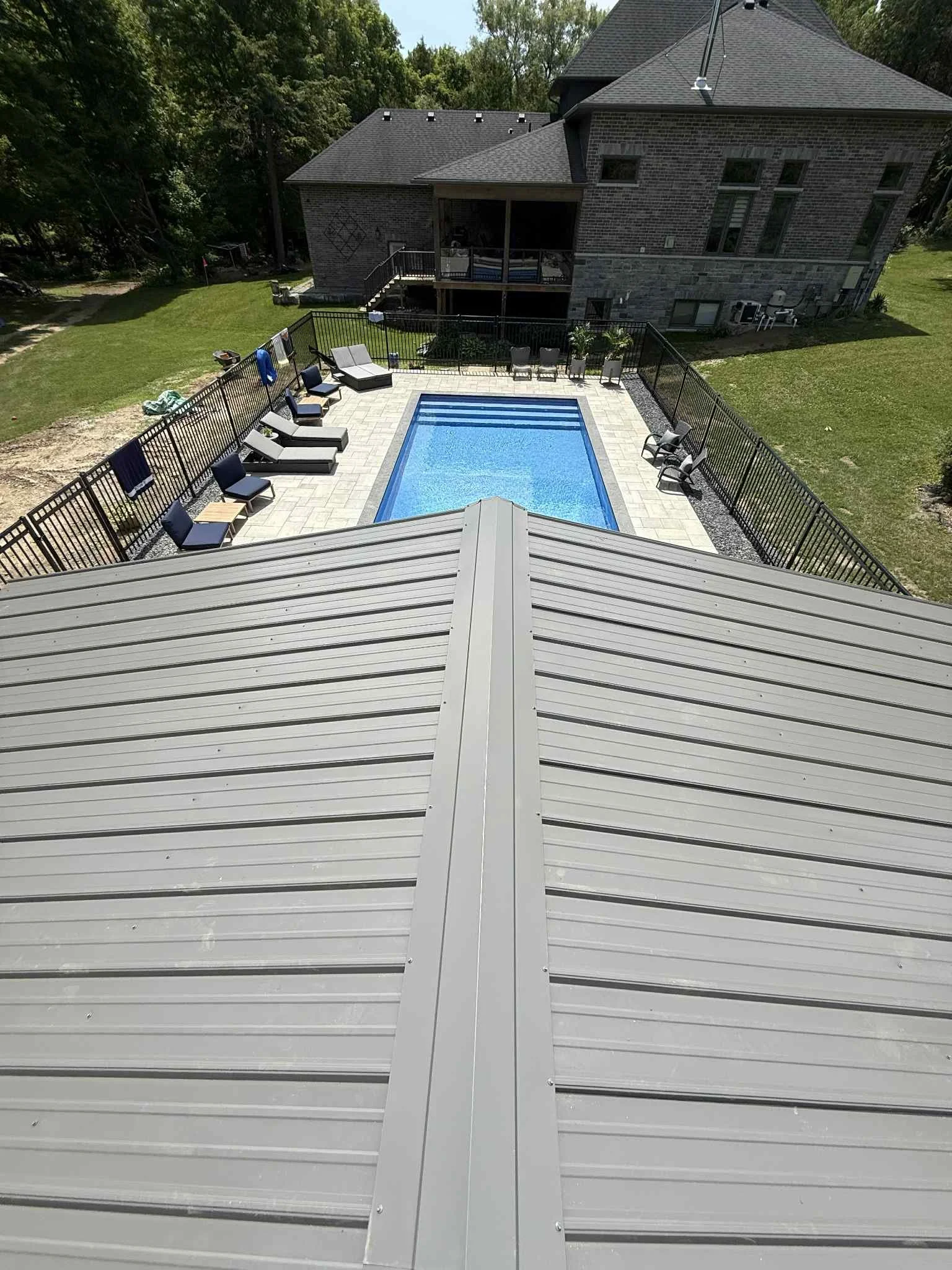 View from above of a backyard with a rectangular in-ground swimming pool surrounded by a patio with lounge chairs and a house in the background.