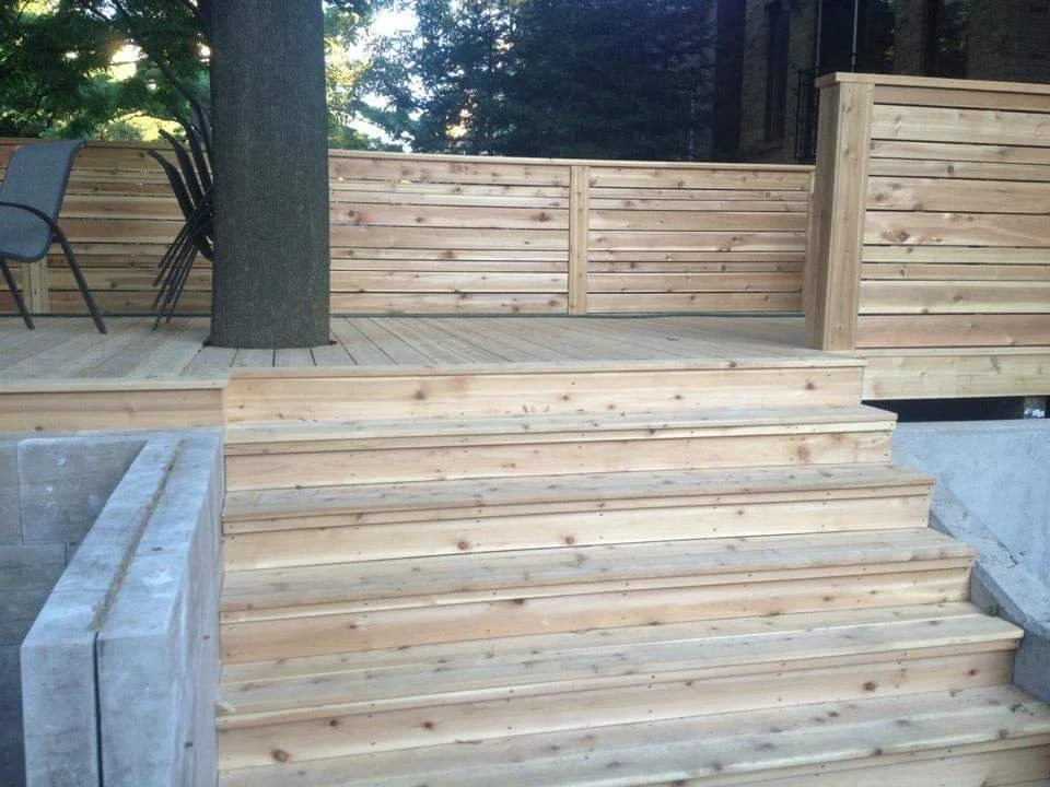 Wooden outdoor deck with stairs and a tree growing through the deck, surrounded by a wooden fence.