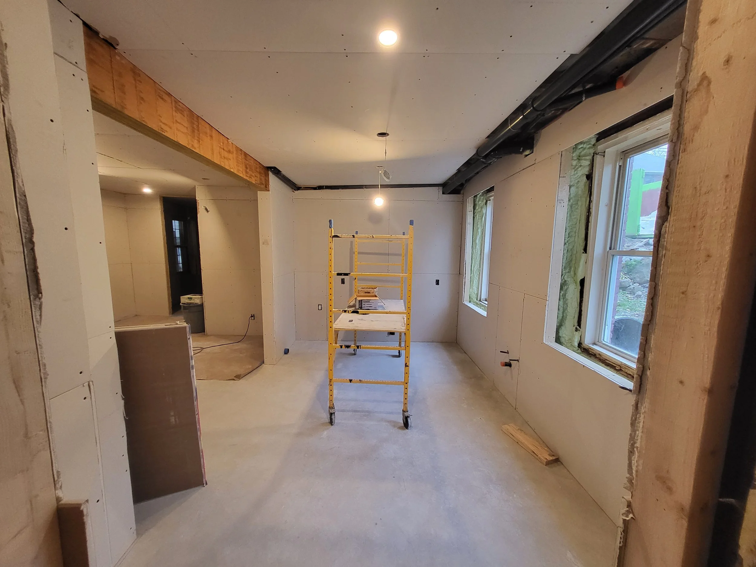 Interior of a house under construction with unfinished walls, a yellow scaffolding in the center, and windows on the right side
