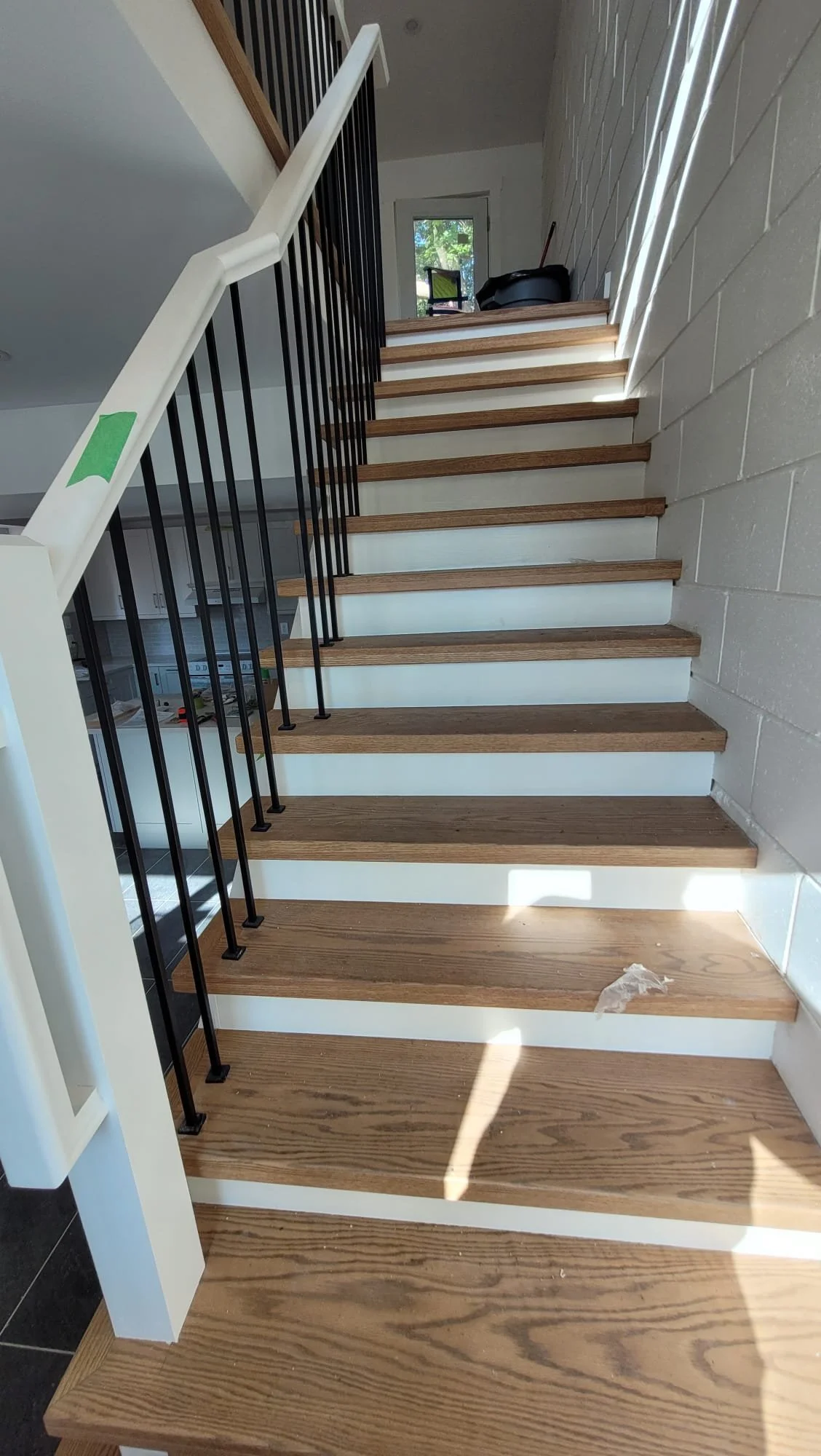 Wooden staircase with black metal balusters and white risers in a modern home, with a window at the top letting in natural light.