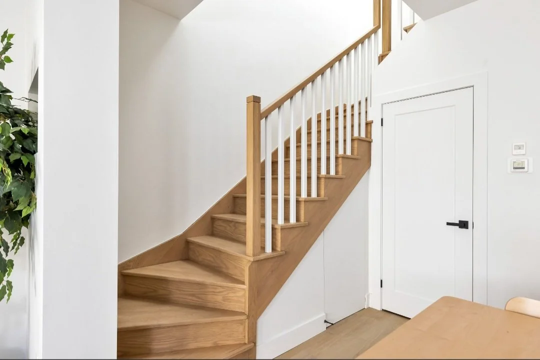 Wooden staircase with white railing and a small closet with a white door underneath, in a bright minimalist home interior.
