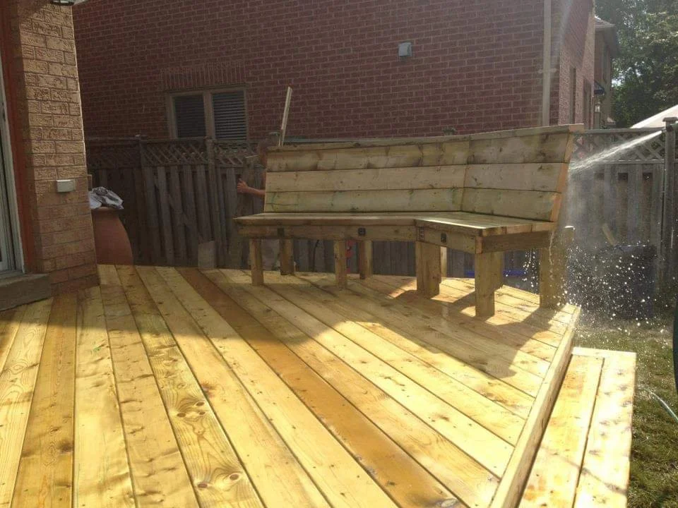 Freshly built wooden deck with a bench and sprinkler watering the area.