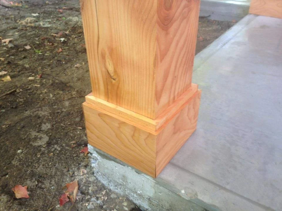 Close-up of a wooden post base on concrete and dirt ground.