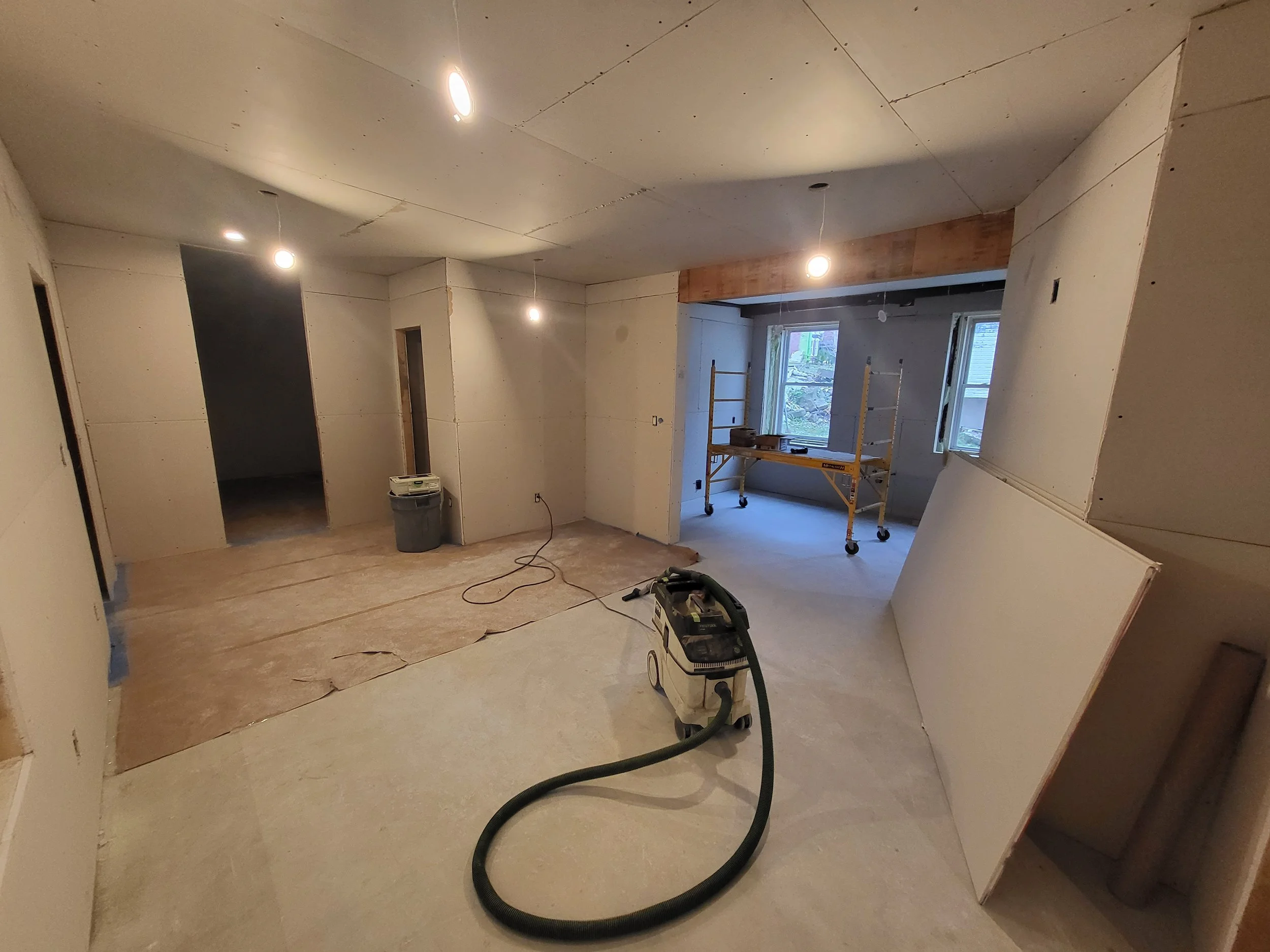 Room under construction with drywall, construction tools, and a vacuum cleaner.