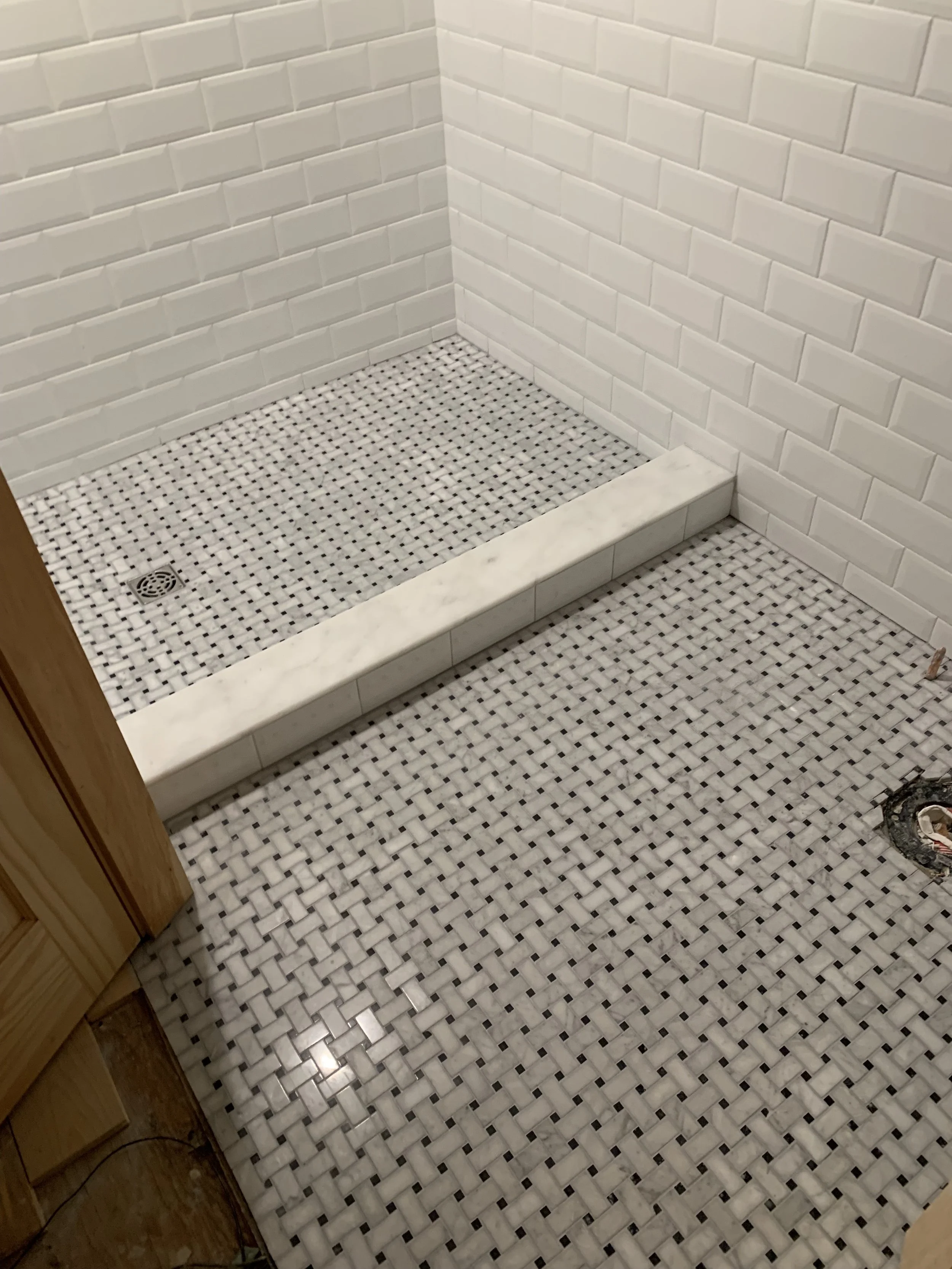 Bathroom shower area with white subway tiles on the walls, a bronze drain on the floor, and a partially finished countertop with marble edges.
