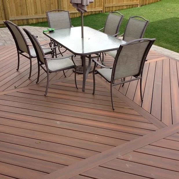 Outdoor dining table with six chairs on a wooden deck in a backyard.