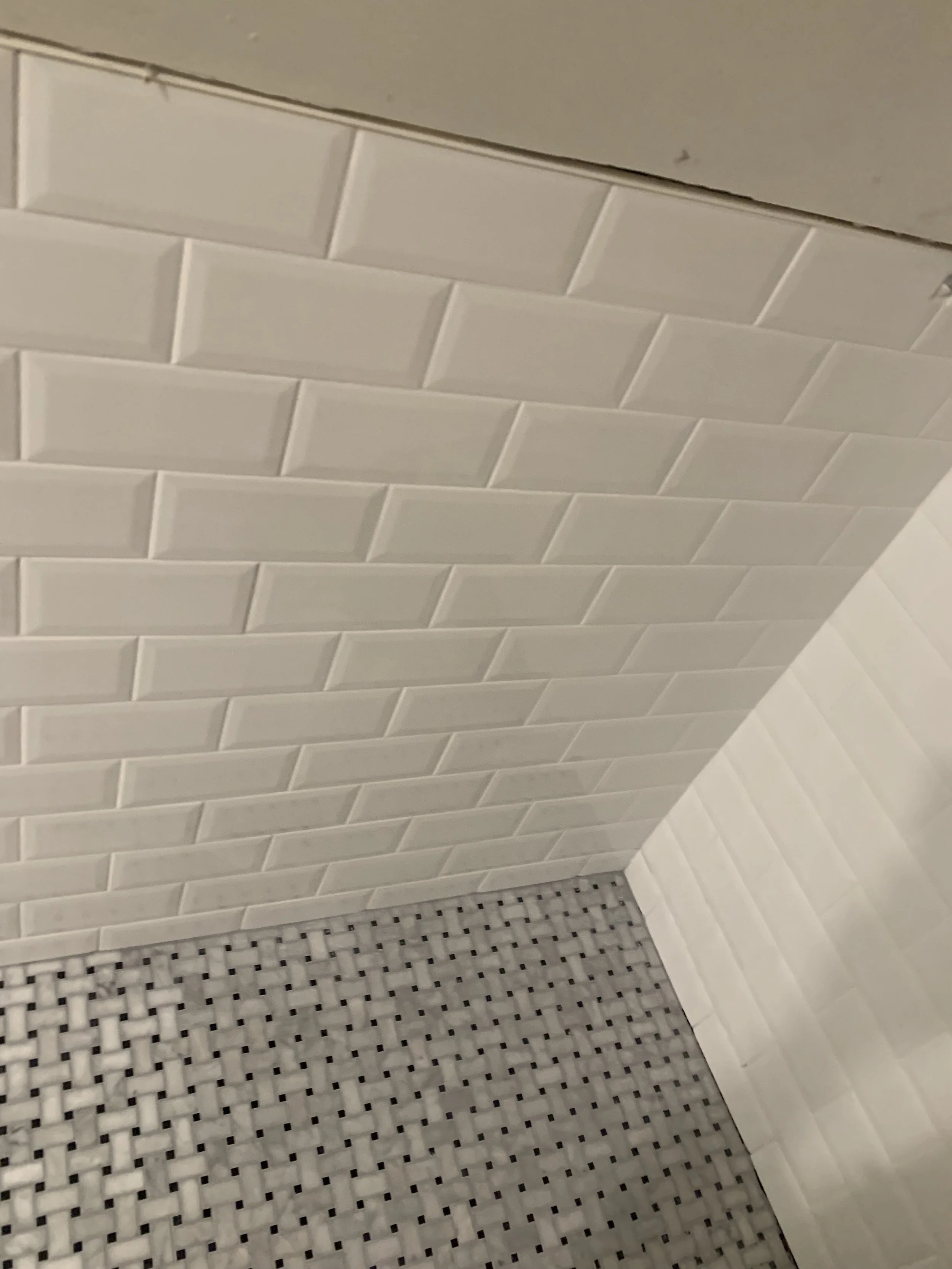 Close-up of a tiled bathroom corner with white subway tiles on the walls and black-and-white mosaic tiles on the floor.