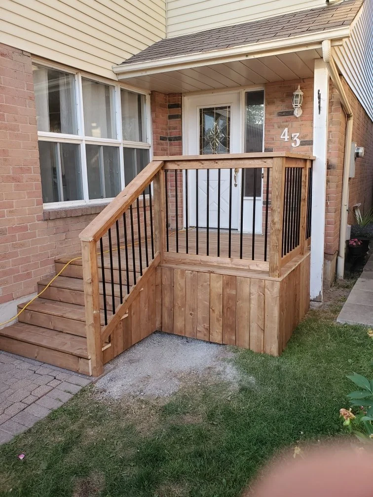 Wooden porch with stairs and railing outside a brick house, with a white door, house number 43, and a porch light.