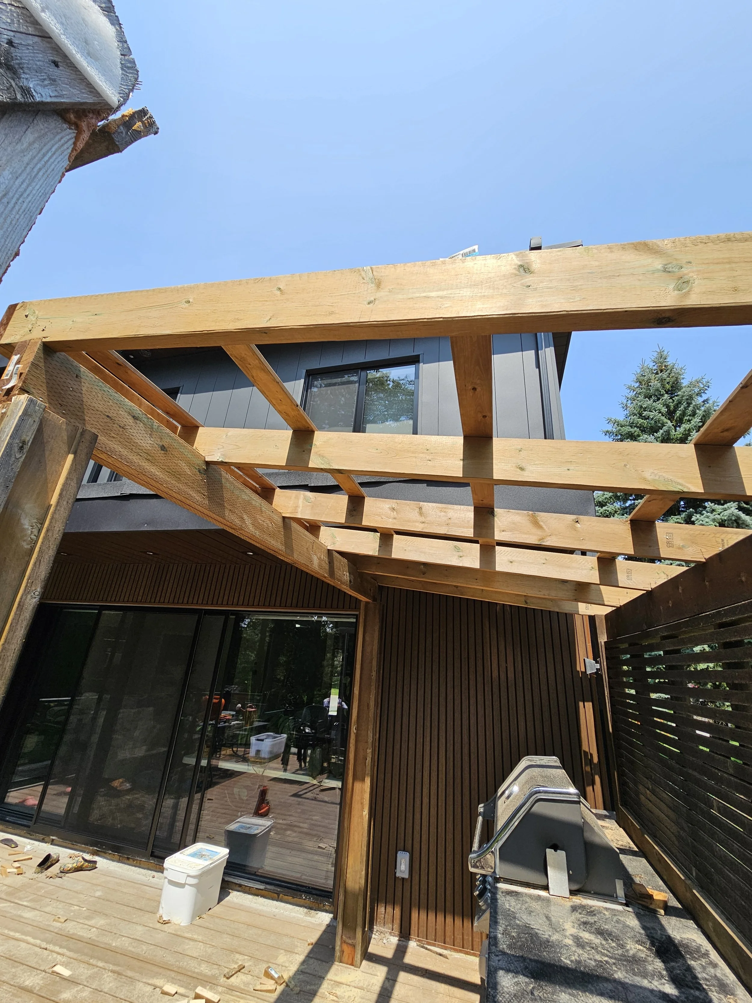 Under construction wooden deck with beams and sliding glass door leading to indoor area.