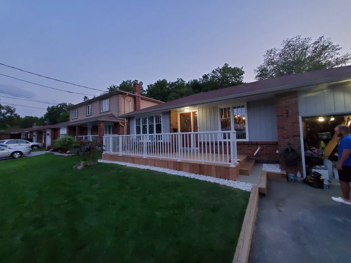 Residential duplex with porch and lawn, person standing near garage with tools, during dusk.