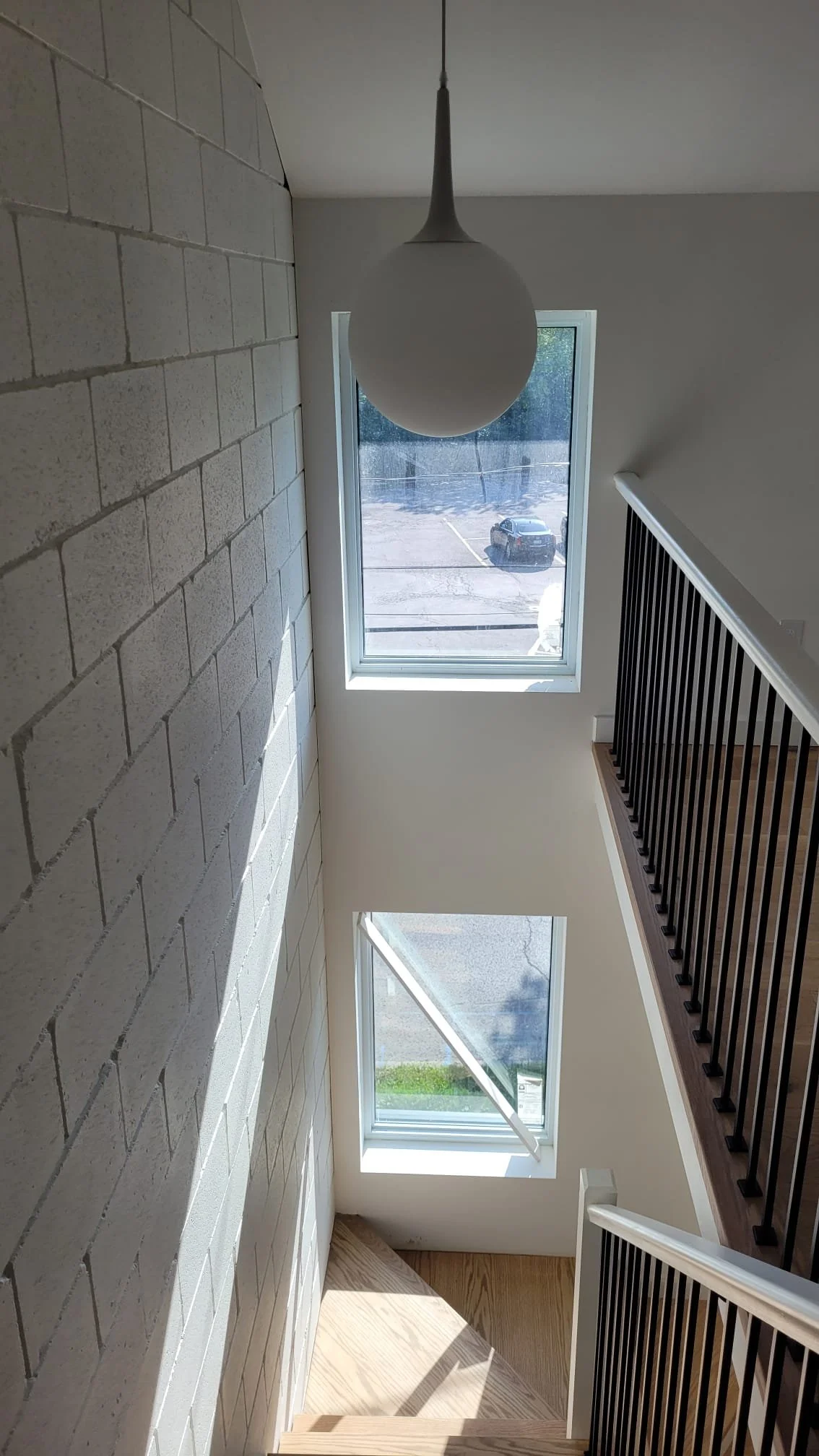 Interior view of a stairway landing with two windows, a hanging spherical white pendant light, and black metal stair railings.