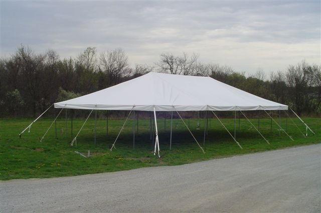 A large white outdoor tent set up on a grassy area, with trees and cloudy sky in the background.