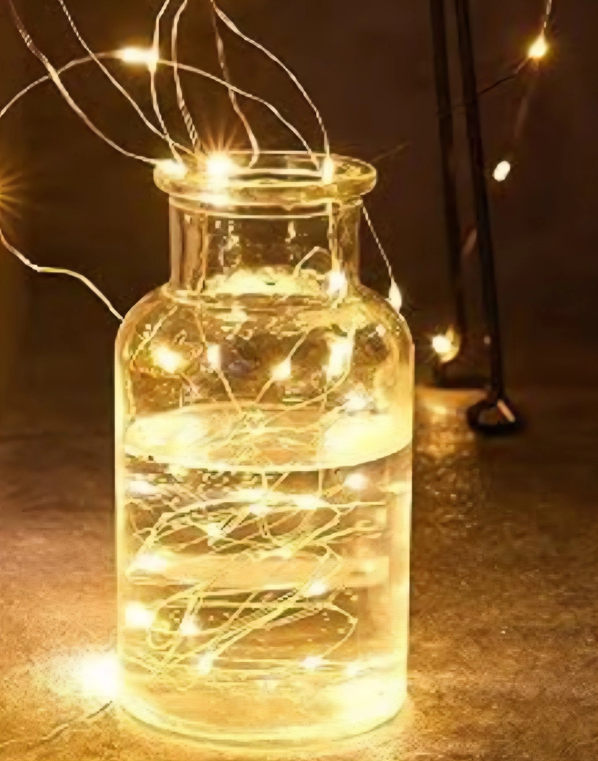A glass jar filled with string lights, creating a glowing effect, placed on a surface with a dark background.