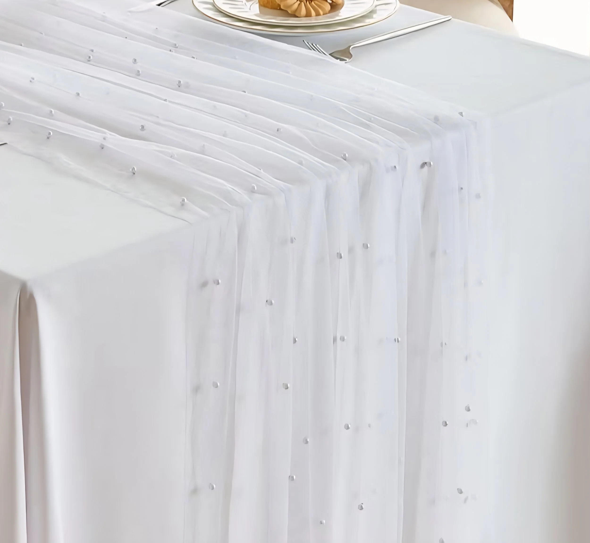 Close-up of a white wedding reception table with a tablecloth adorned with small decorative embellishments.