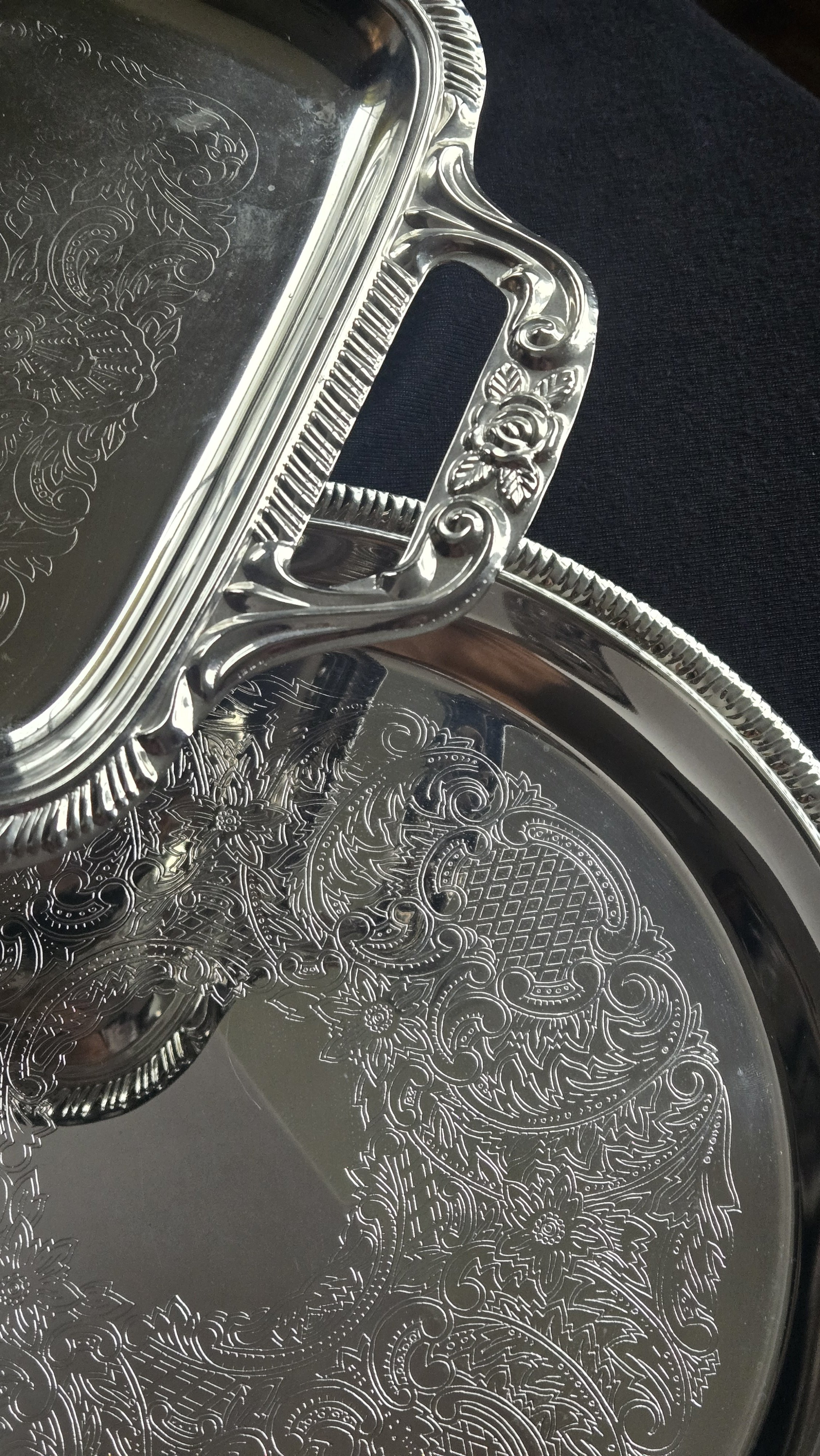Close-up of ornate engraved silver serving tray and lid with floral patterns and decorative details, resting on a dark surface.