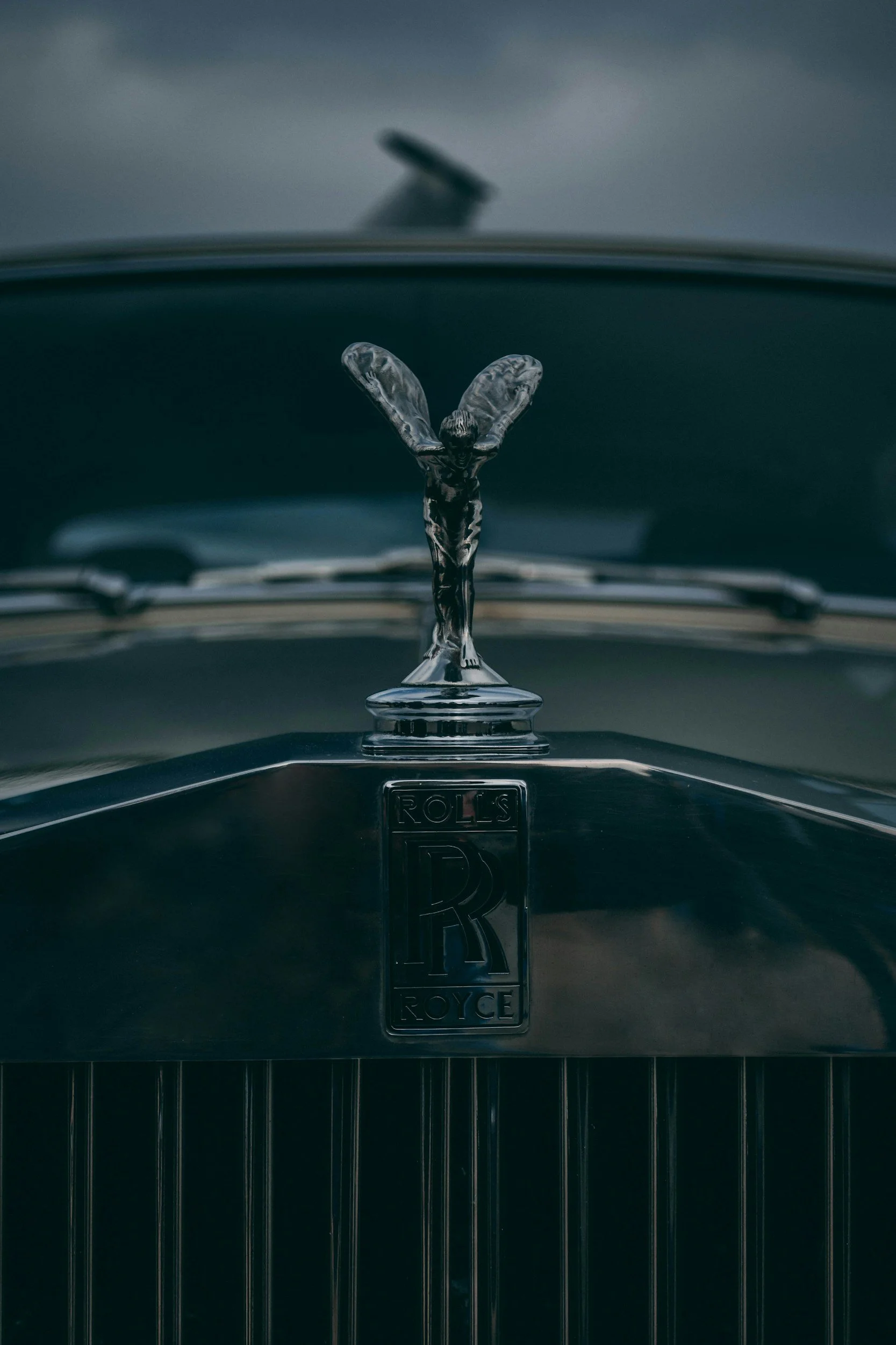 Close-up of a vintage Rolls-Royce car hood ornament, the Spirit of Ecstasy, with the Rolls-Royce emblem below.