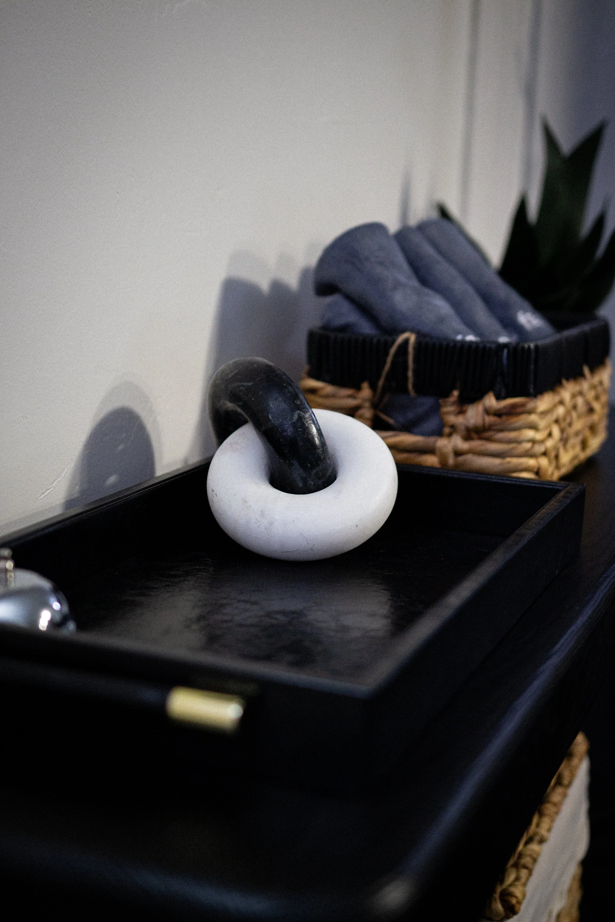 Decorative black and white stone sculpture on a black tray, with a woven basket containing folded gray socks and a plant in the background.