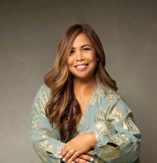 A woman with long, wavy hair smiling and posing with arms crossed against a gradient background.