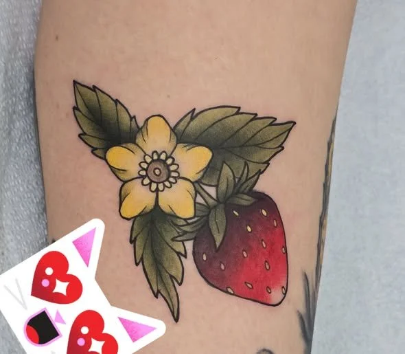 Tattoo of a yellow flower, green leaves, and a red strawberry on skin.