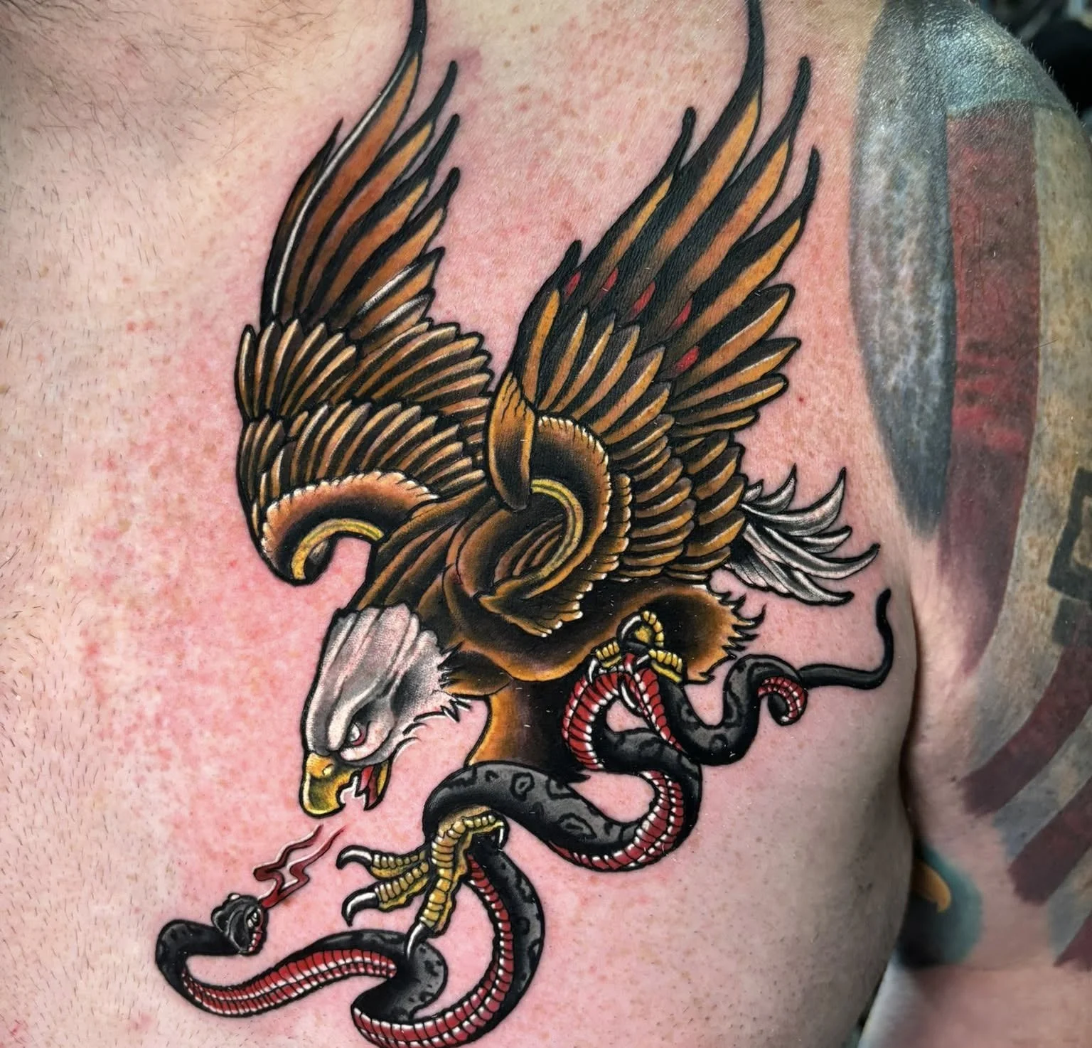 Tattoo of a bald eagle with outstretched wings gripping a black and red snake in its talons.