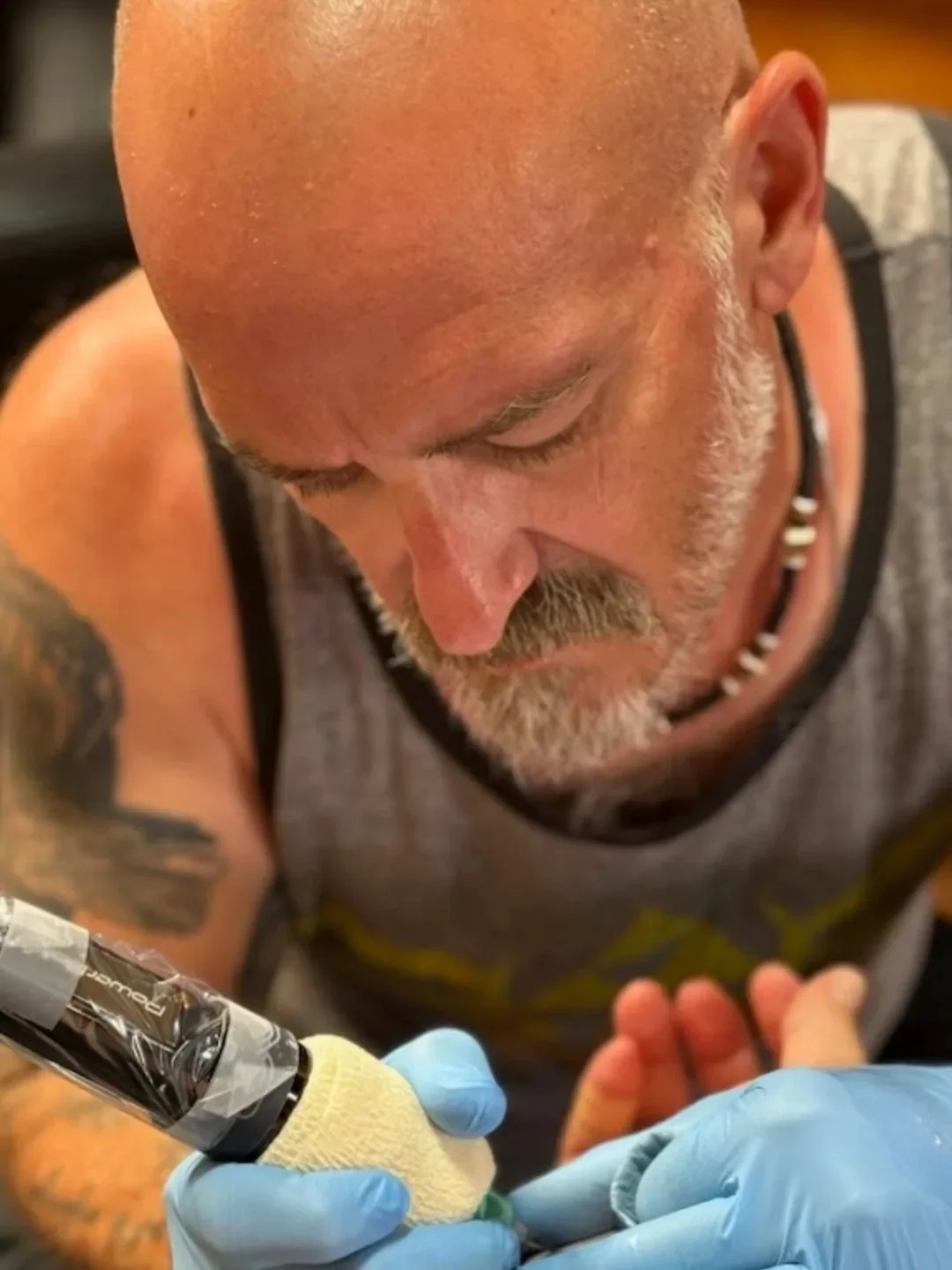 A man receiving a tattoo from a tattoo artist wearing blue gloves.