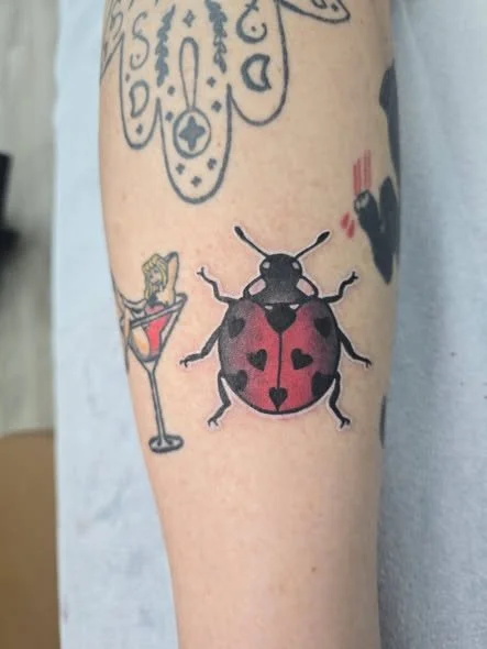Tattoo of a lady in a red dress sitting in a cocktail glass, with a ladybug that has red wings and black spots.