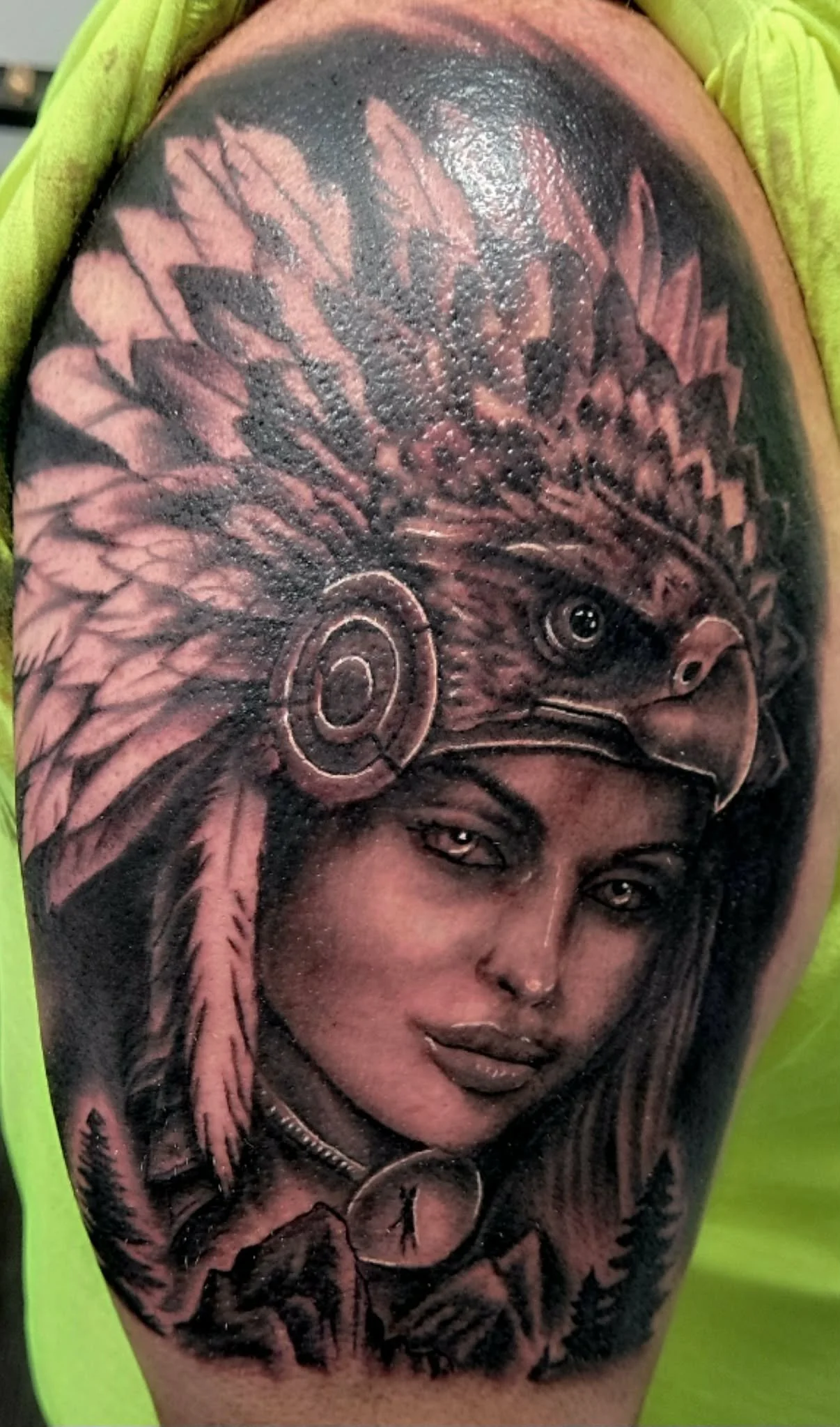 A detailed black and gray tattoo of a woman wearing a Native American headdress with a hawk face and headphones, surrounded by nature elements.