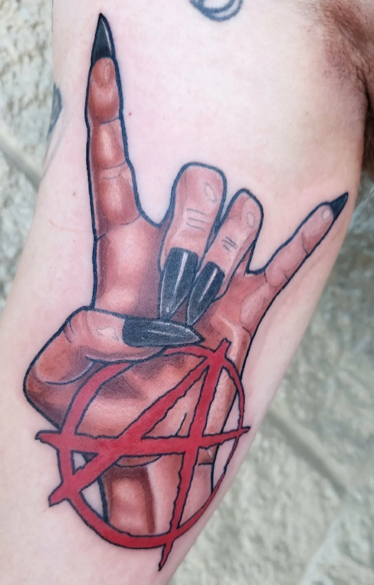Tattoo of a realistic anatomical heart with a hand making the sign of the horns, outlined with a red pentagram.