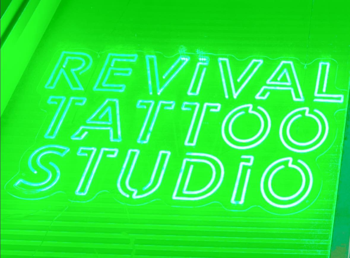 Neon sign that reads 'REVIVAL TATTOO STUDIO' in blue on a green background.
