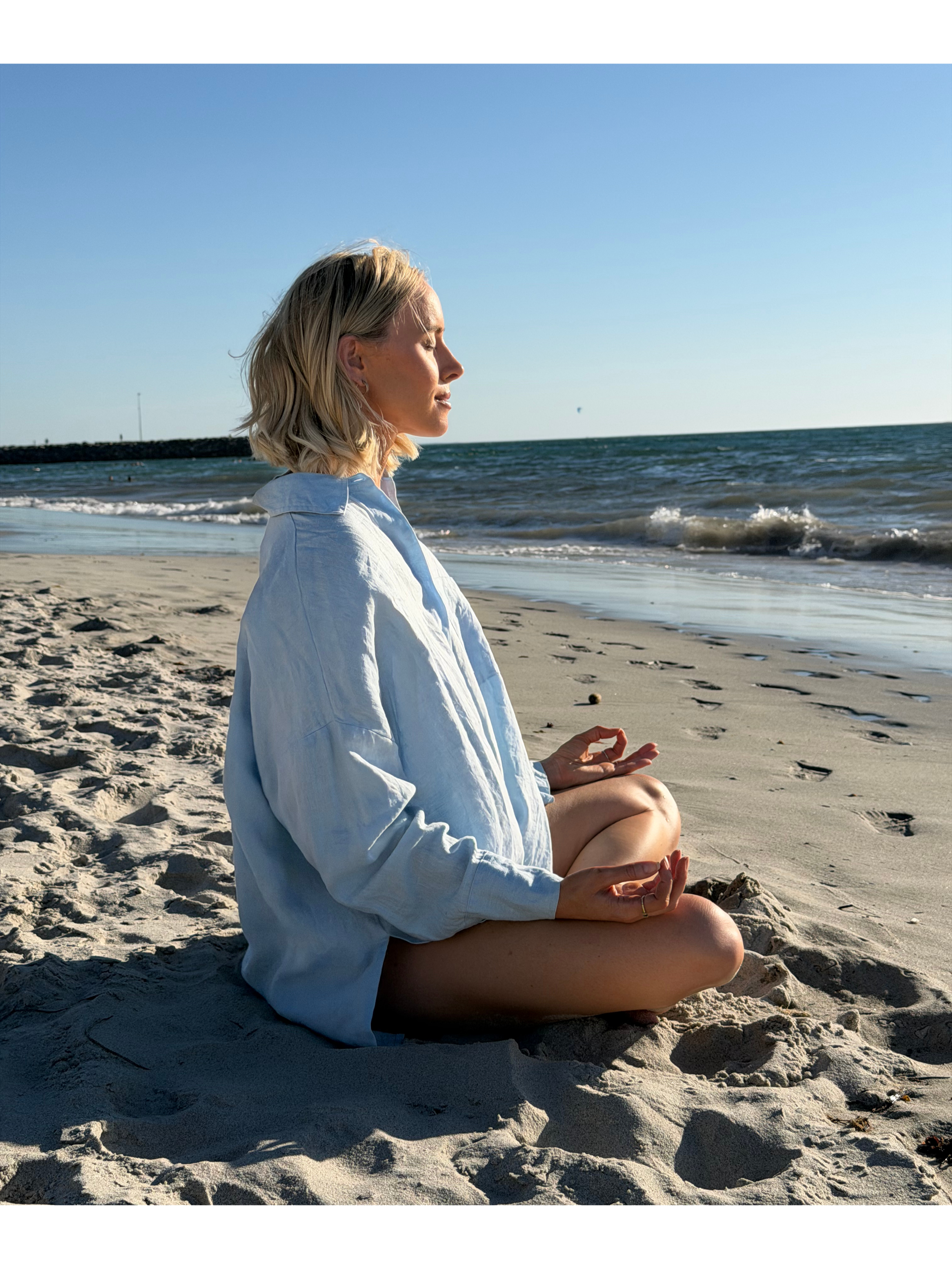 Woman practicing meditation on a sandy beach with the ocean in the background.